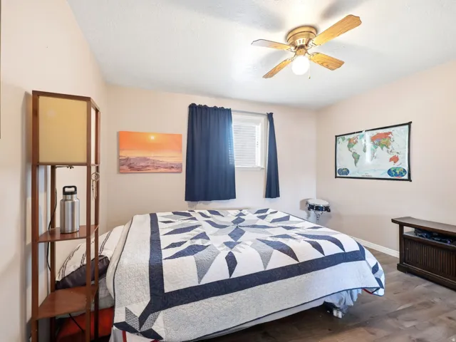 Bedroom featuring wood-finish flooring, a ceiling fan with integrated lighting, and a window with blinds