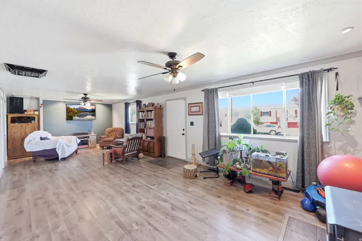Spacious living area featuring wood-finish flooring, a large window, and multiple ceiling fans