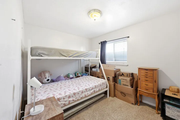 Carpeted room featuring a white bunk bed, a single window with blinds and dark curtains, and a ceiling-mounted light fixture