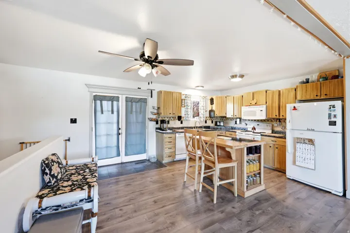 Spacious kitchen featuring wood-finish flooring, light wood cabinetry, white appliances, and a central island with integrated shelving