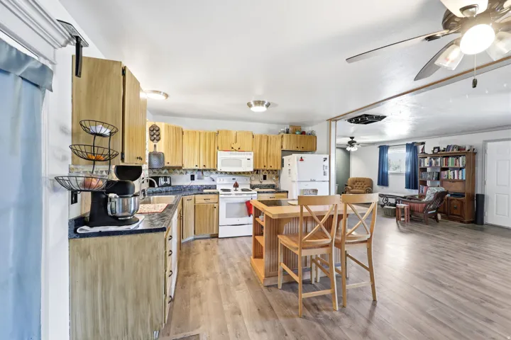 Kitchen featuring wood-finish cabinetry, dark countertops, white appliances, and a central island with seating