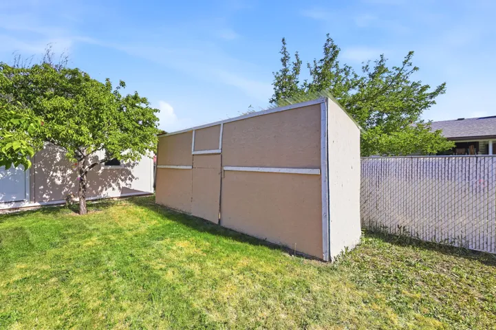 Backyard storage shed with paneled construction and a chain-link fence border