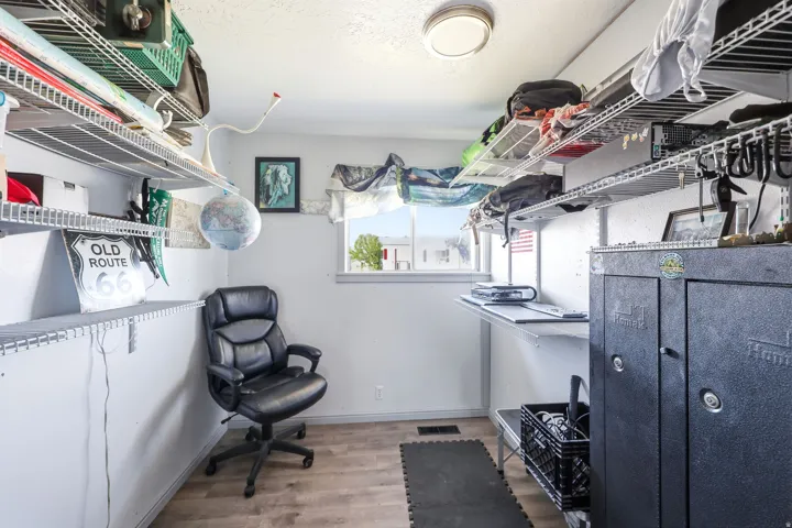 Office space featuring wood-finish flooring, a flush-mount ceiling light, a window with a white frame, and extensive wire shelving