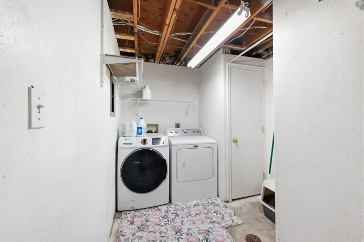 Dedicated laundry area featuring exposed wood ceiling joists, overhead fluorescent lighting, a white wire shelf, and a white interior door