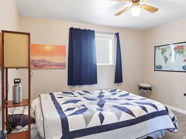 Spacious room featuring wood-finish flooring, a window with blinds and drapes, and a ceiling fan with integrated lighting