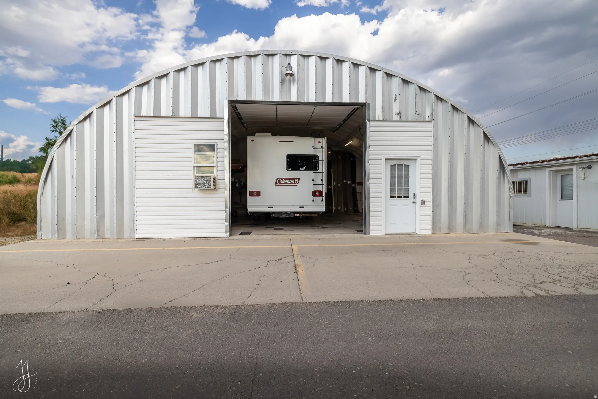 Quonset hut-style metal building featuring a large overhead door, white vinyl siding accents, a glass panel pedestrian door, and a window with an air conditioning unit