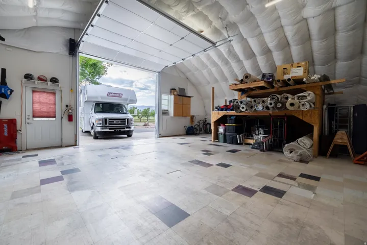 Spacious garage with a large overhead door, durable tiled flooring, insulated ceiling, and a separate entry door