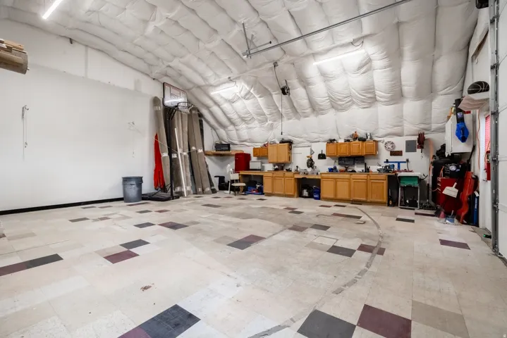 Spacious garage with a high, insulated ceiling, fluorescent lighting, and a workbench with wood cabinetry
