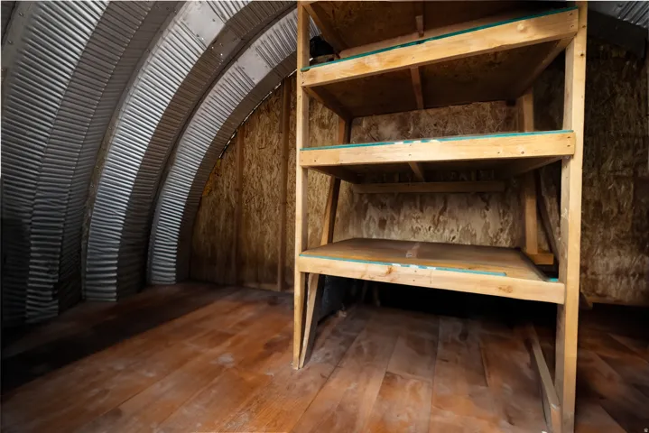 Interior space featuring a corrugated metal arched ceiling, wood-finish flooring, oriented strand board (OSB) wall panels, and built-in wood shelving