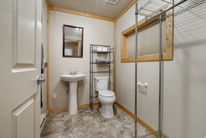 Pedestal sink with chrome faucet, toilet, and wood-framed window, all set on patterned flooring