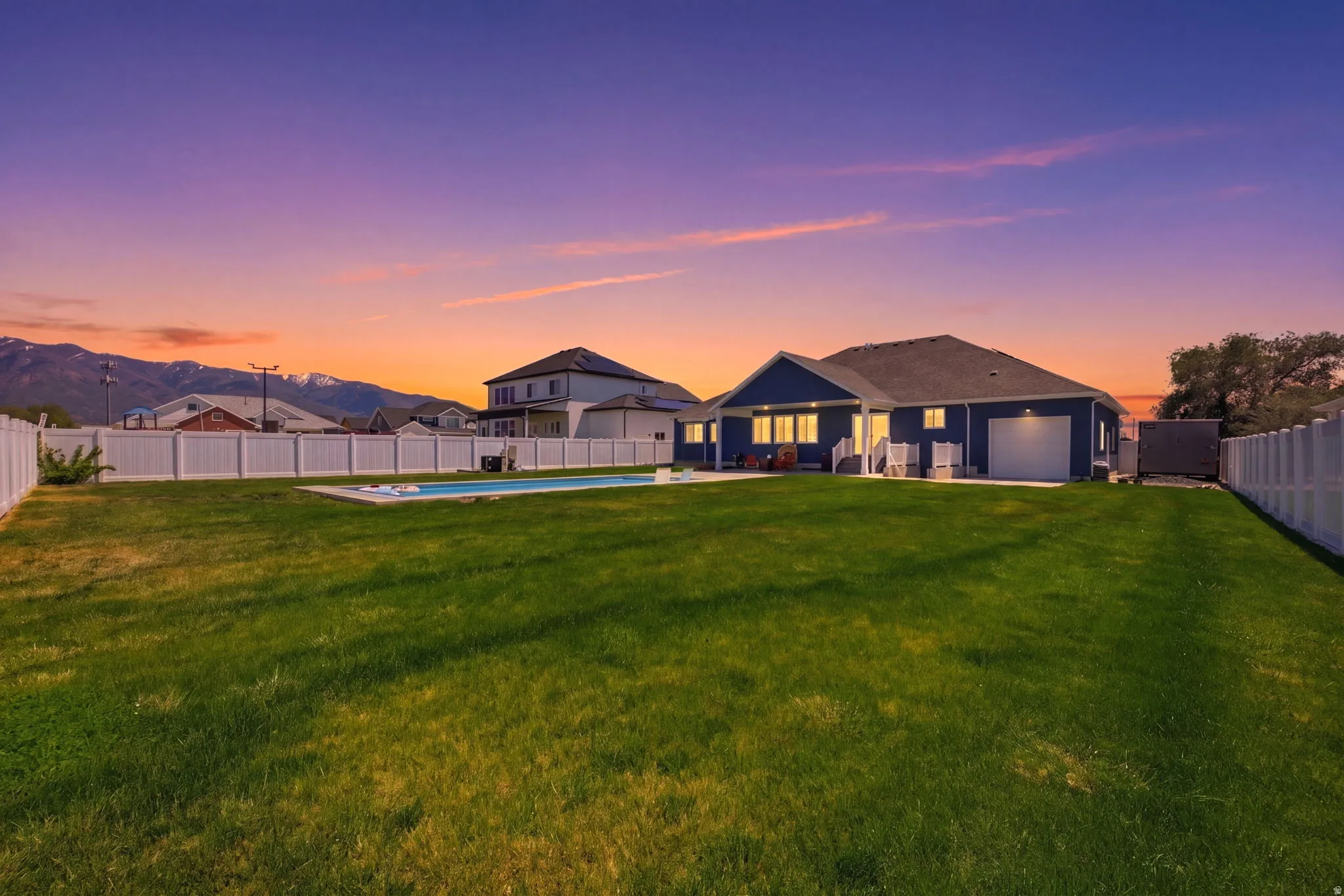 Expansive backyard featuring a manicured lawn, an in-ground swimming pool, and a white picket fence enclosing the perimeter