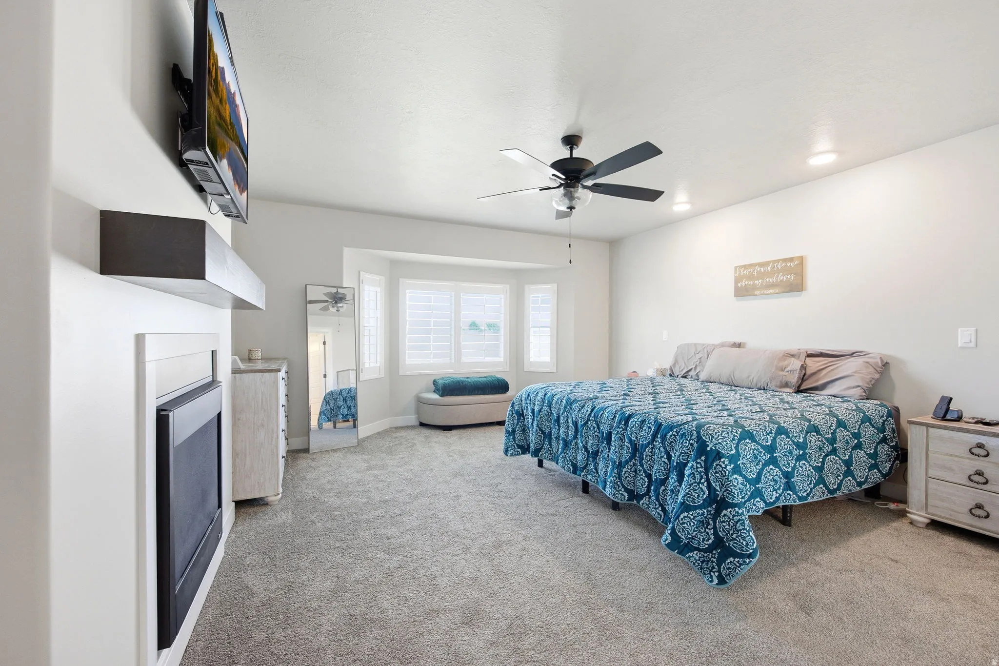 Spacious main bed room featuring a bay window with integrated seating, a ceiling fan with integrated lighting, recessed lighting, and a built-in fireplace with a floating mantel