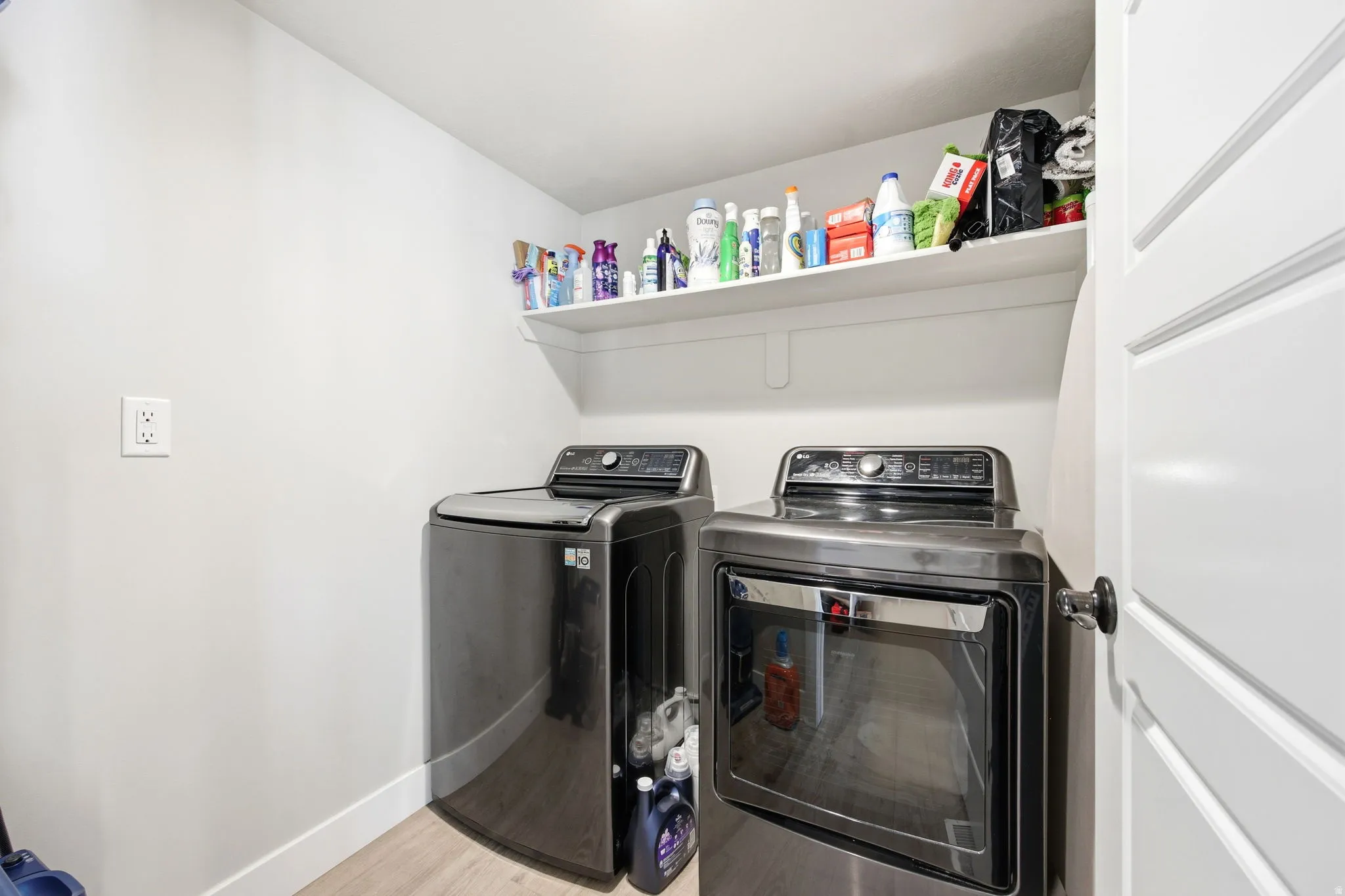 Dedicated laundry area featuring a wall-mounted shelf, light wood-finish flooring, and a white interior door with a black handle