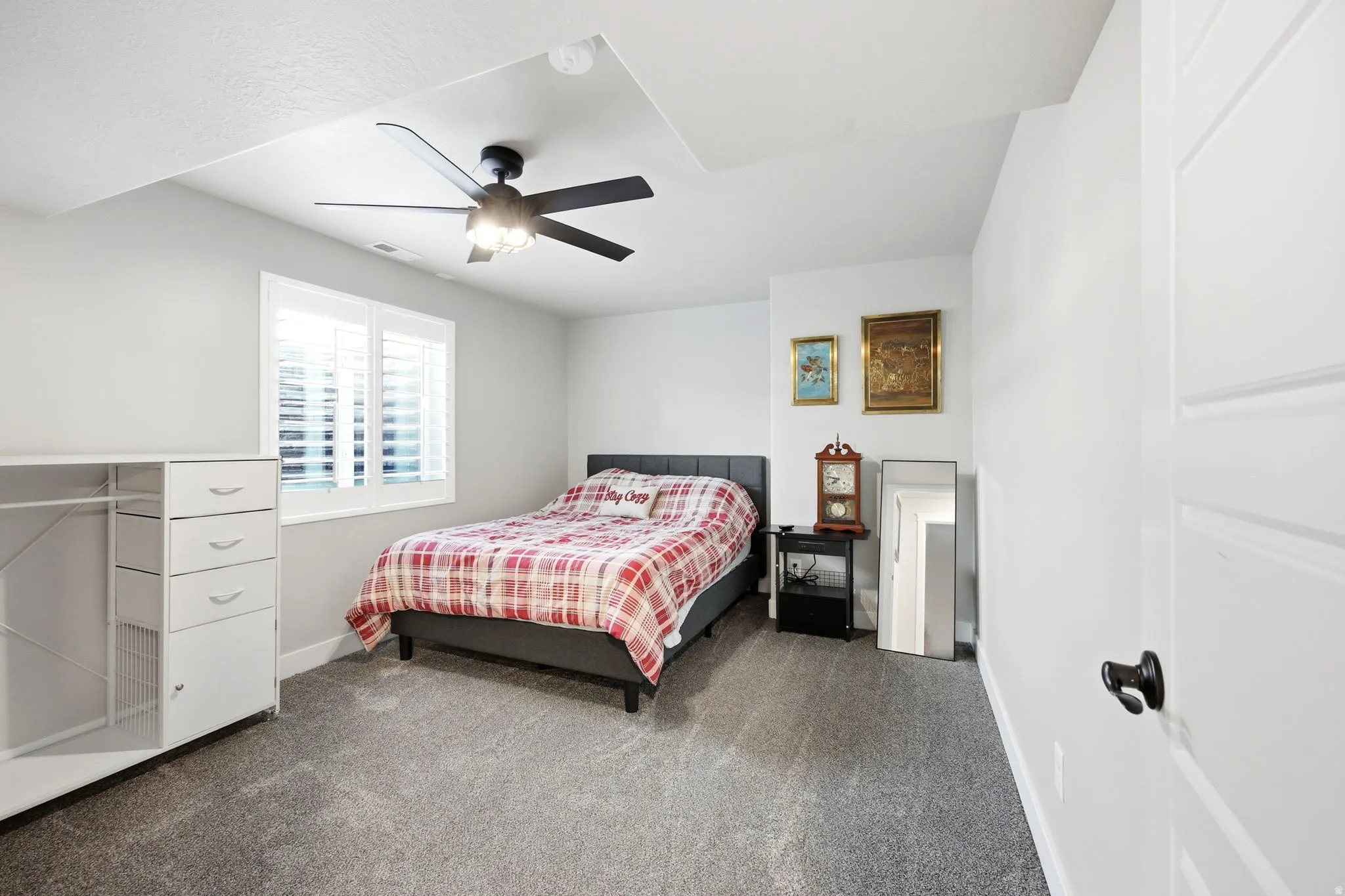 Carpeted room featuring a ceiling fan with integrated lighting, a window with plantation shutters, and a paneled door with dark hardware