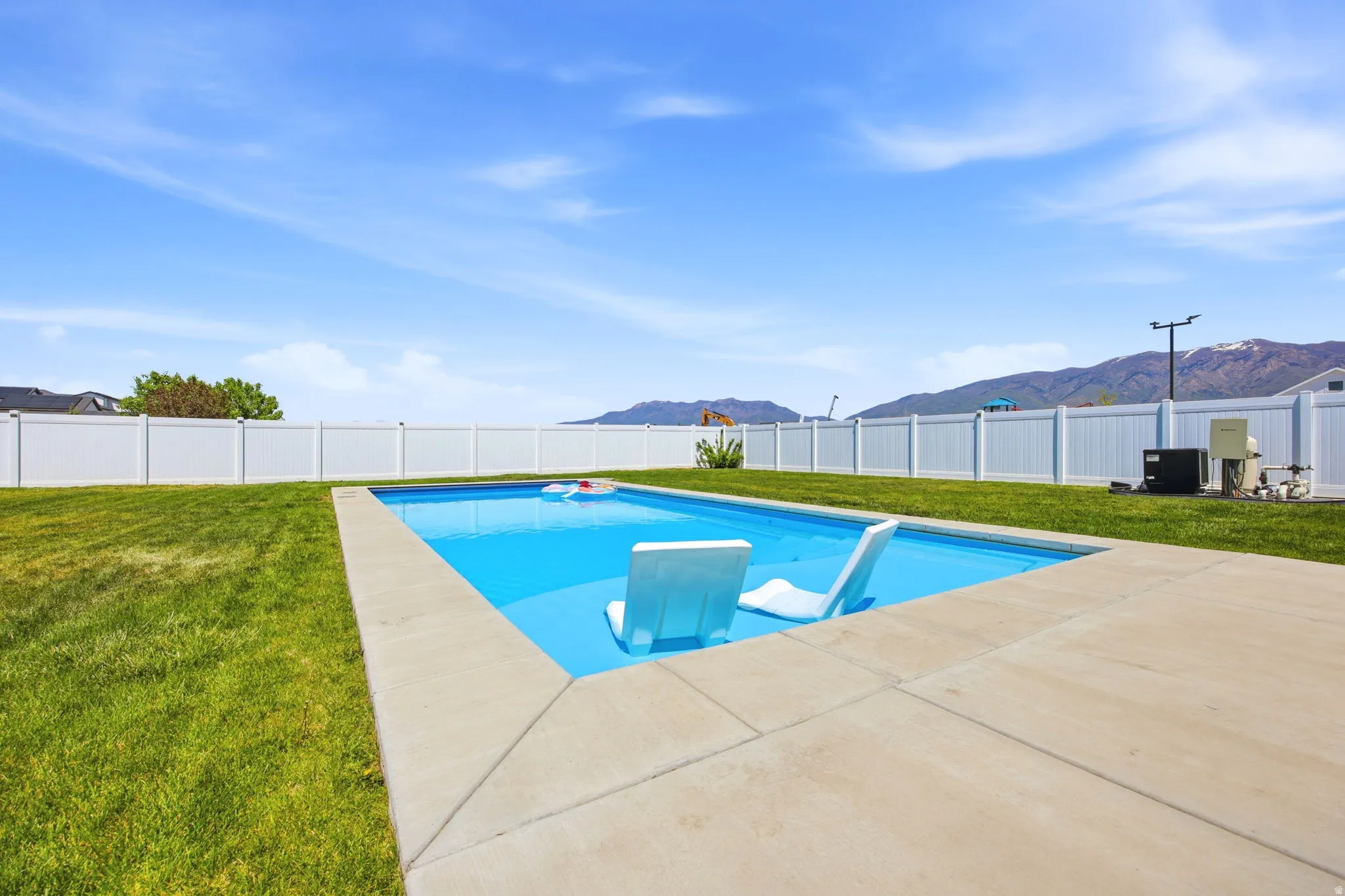 In-ground swimming pool featuring a concrete surround, surrounded by a green lawn and a white vinyl fence