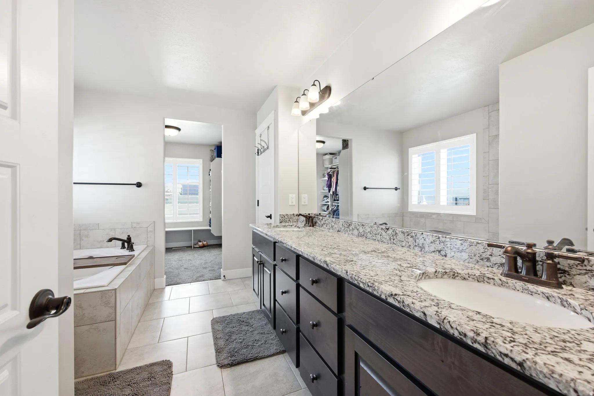 Bathroom featuring a double vanity with stone countertops, a large framed mirror, and a built-in bathtub with tiled surround