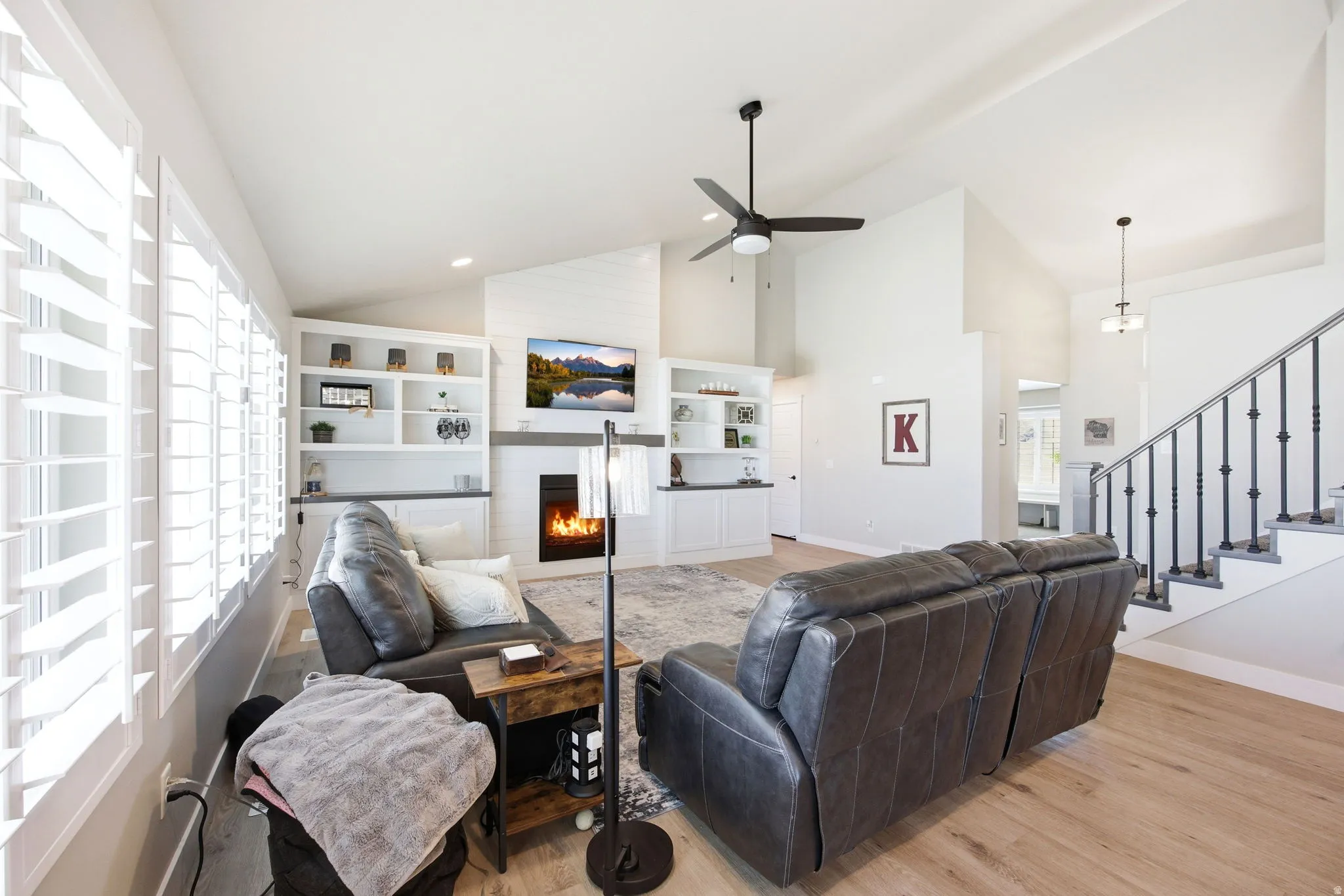 Spacious living area featuring high vaulted ceilings, light wood-finish flooring, and white plantation shutters