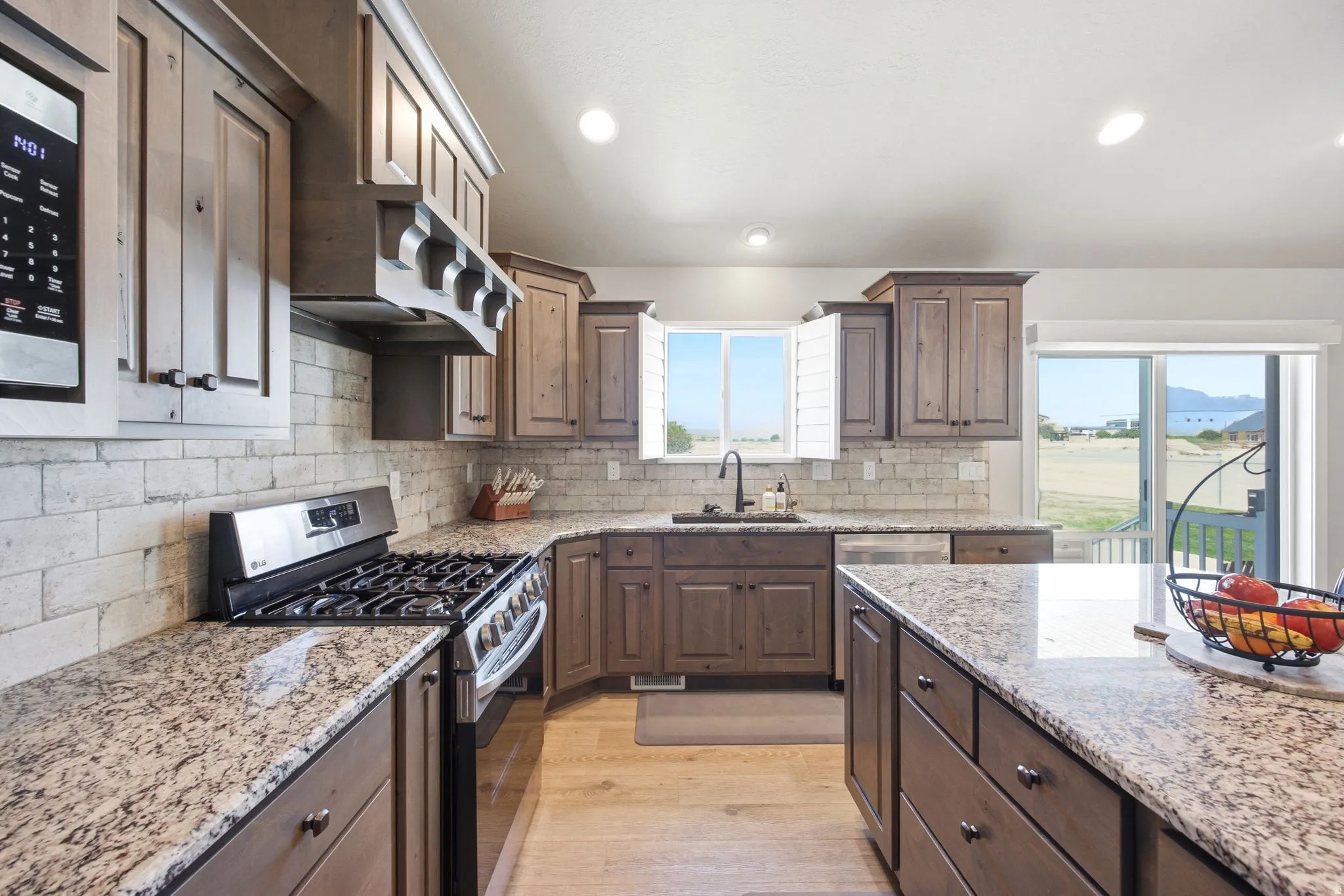 Modern kitchen featuring a gas range, stainless steel appliances, light wood-finish flooring, granite countertops, and a subway tile backsplash
