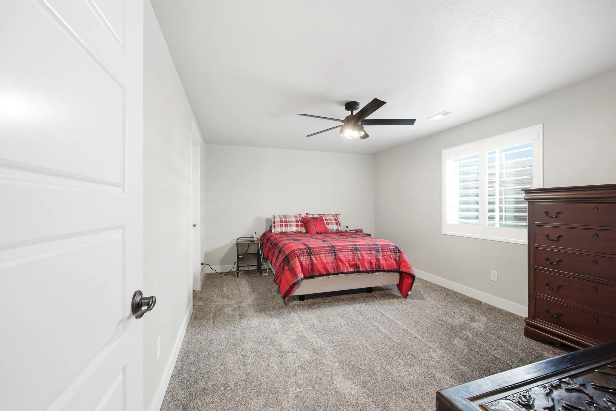 Carpeted room featuring light gray walls, a window with plantation shutters, white baseboards, and a ceiling fan with integrated lighting