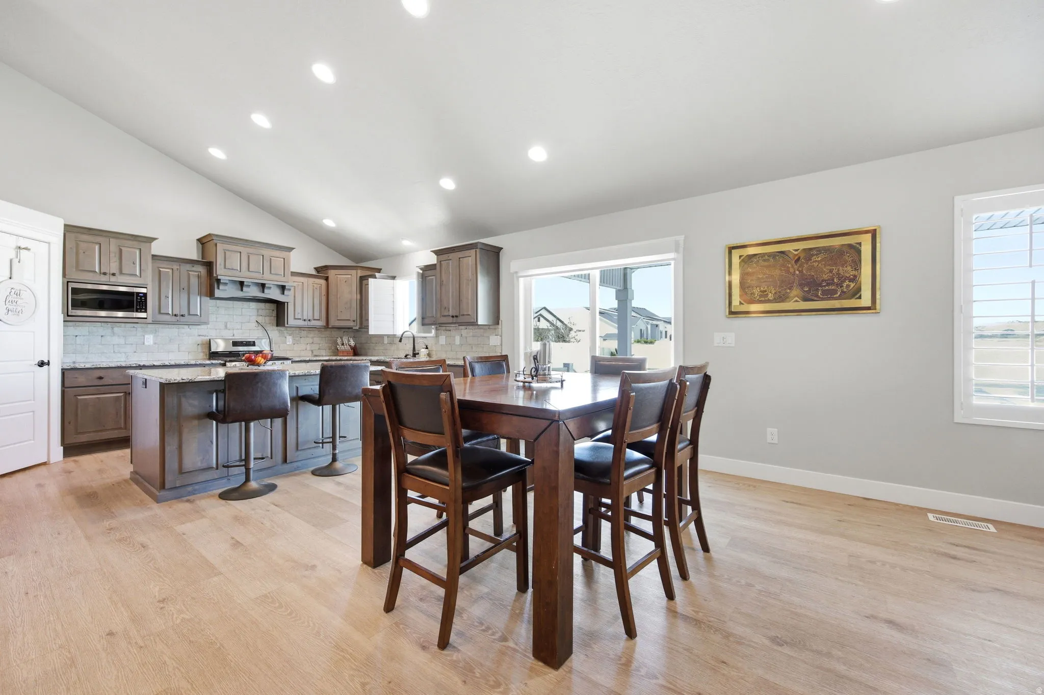 Vaulted ceiling kitchen featuring wood-finish flooring, shaker-style cabinetry, a kitchen island with seating, a tile backsplash, and stainless steel appliances