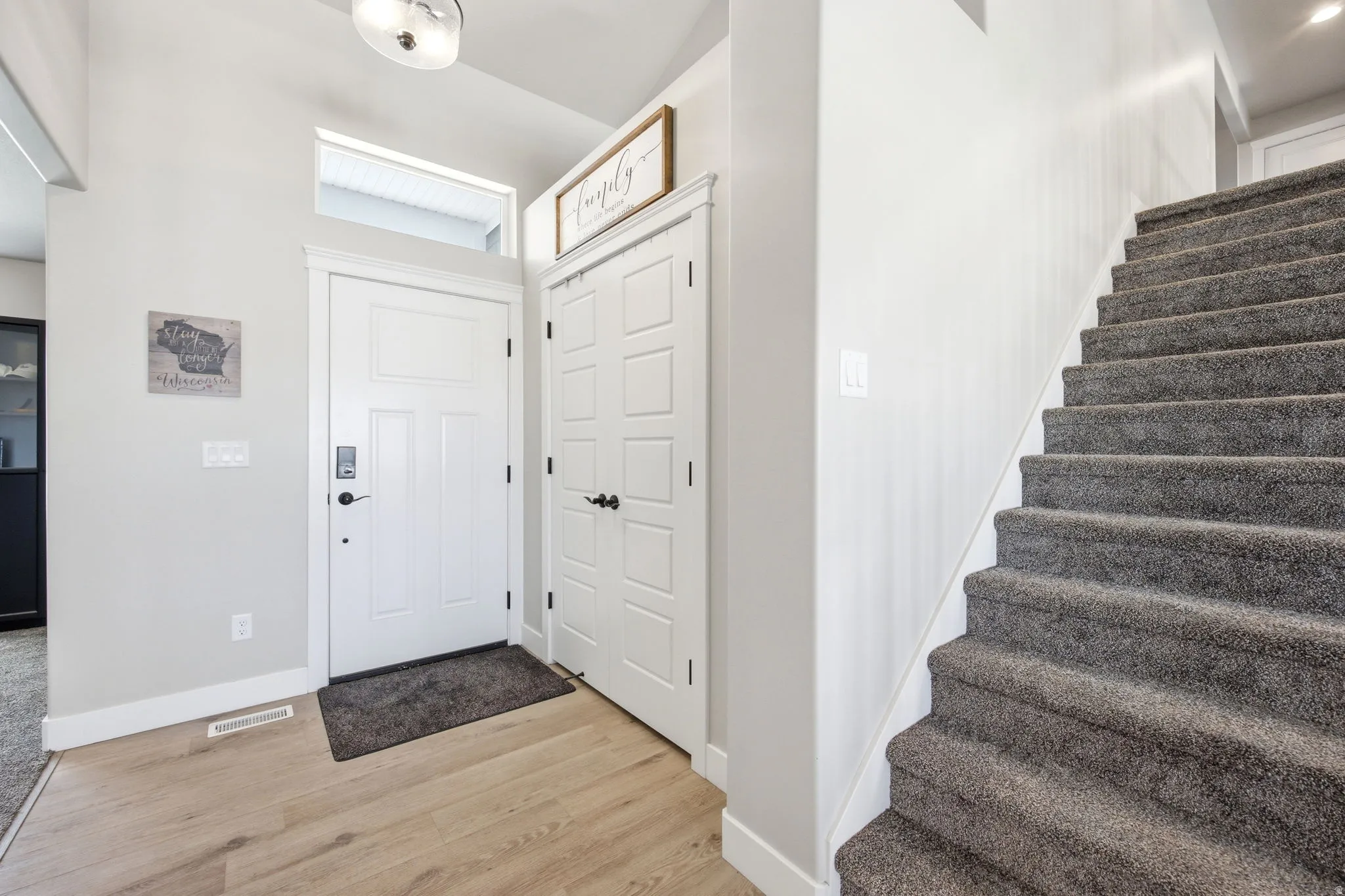 Entryway featuring a light wood-finish flooring, a white front door with transom window, and a built-in closet with paneled doors