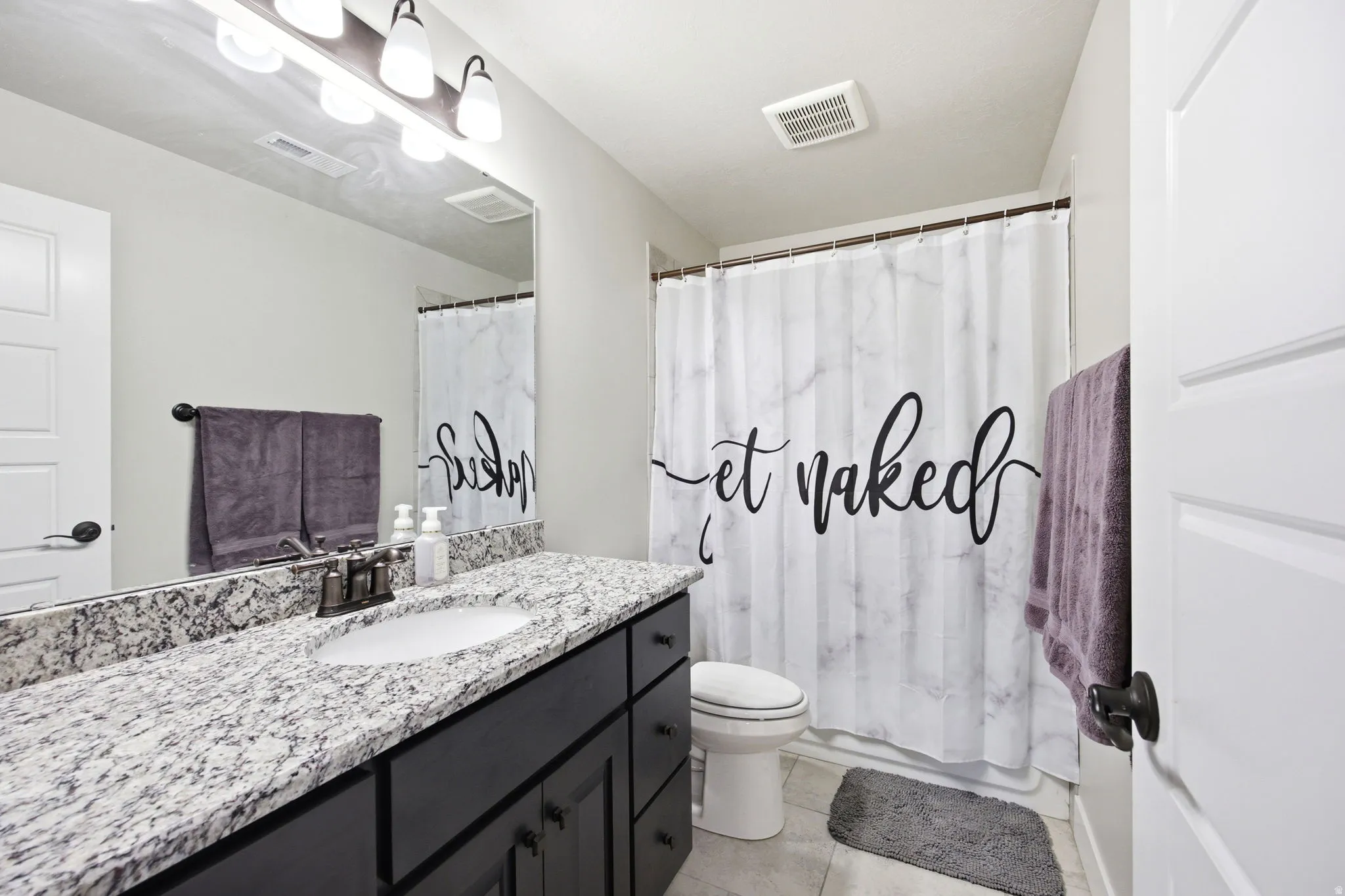 Bathroom featuring a single vanity with stone-finish countertop, undermount sink, and dark cabinetry