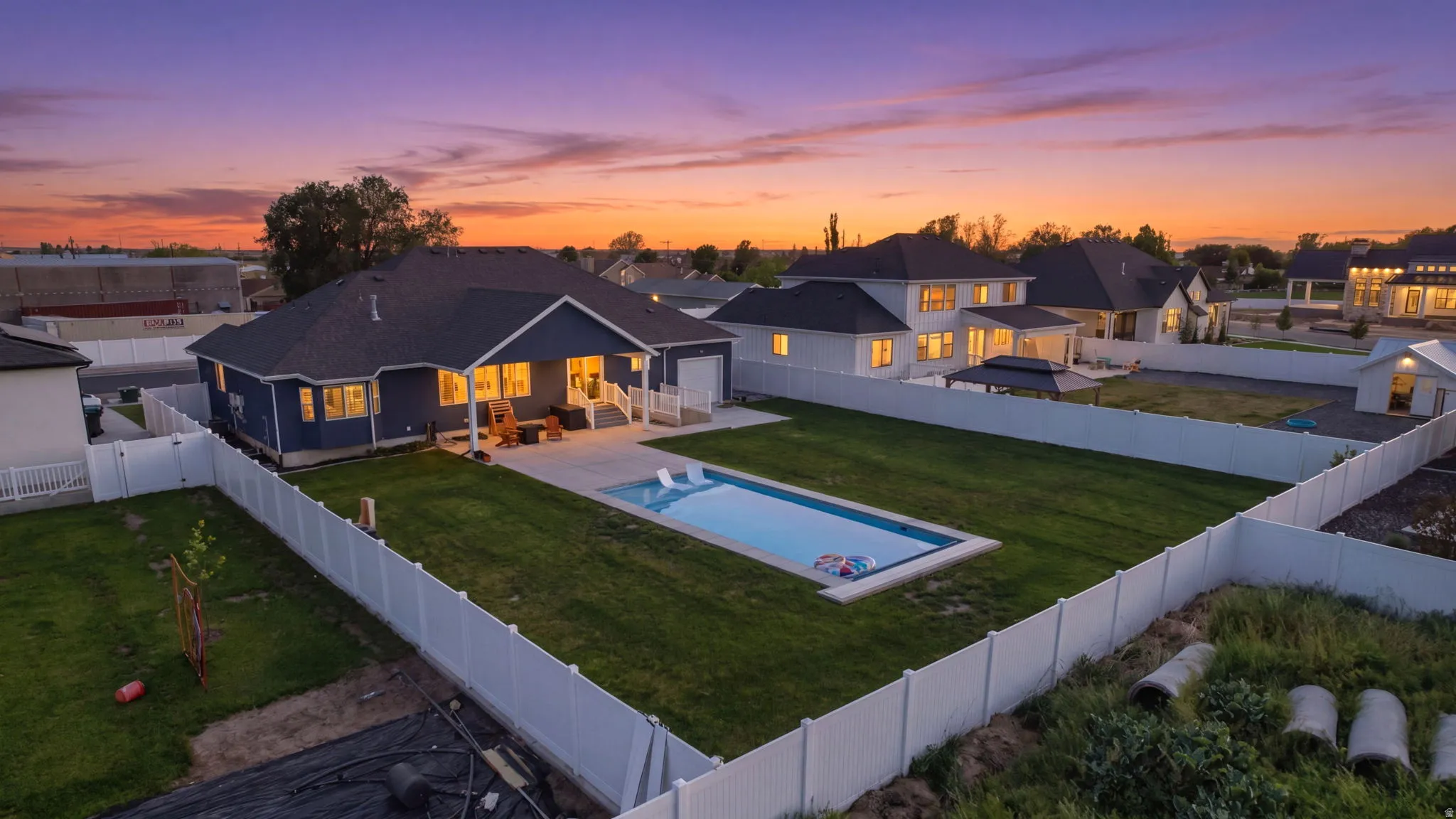 Expansive backyard featuring a rectangular swimming pool with integrated lighting, a manicured lawn, and a white vinyl privacy fence