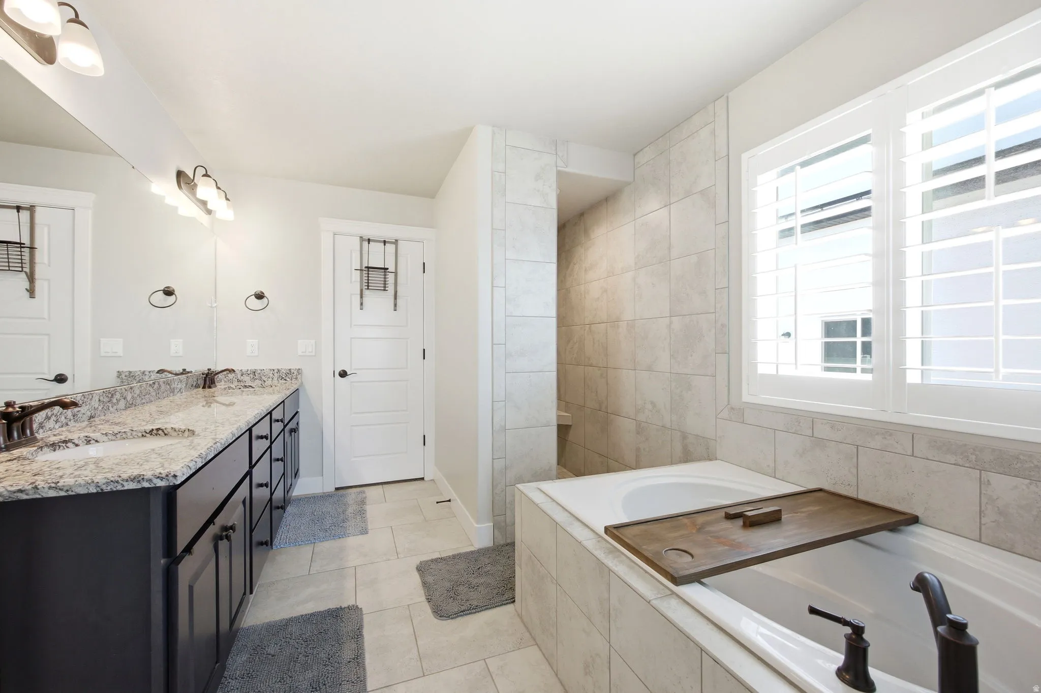 Bathroom featuring a dual vanity with granite countertops, built-in soaking tub, and a separate tiled shower