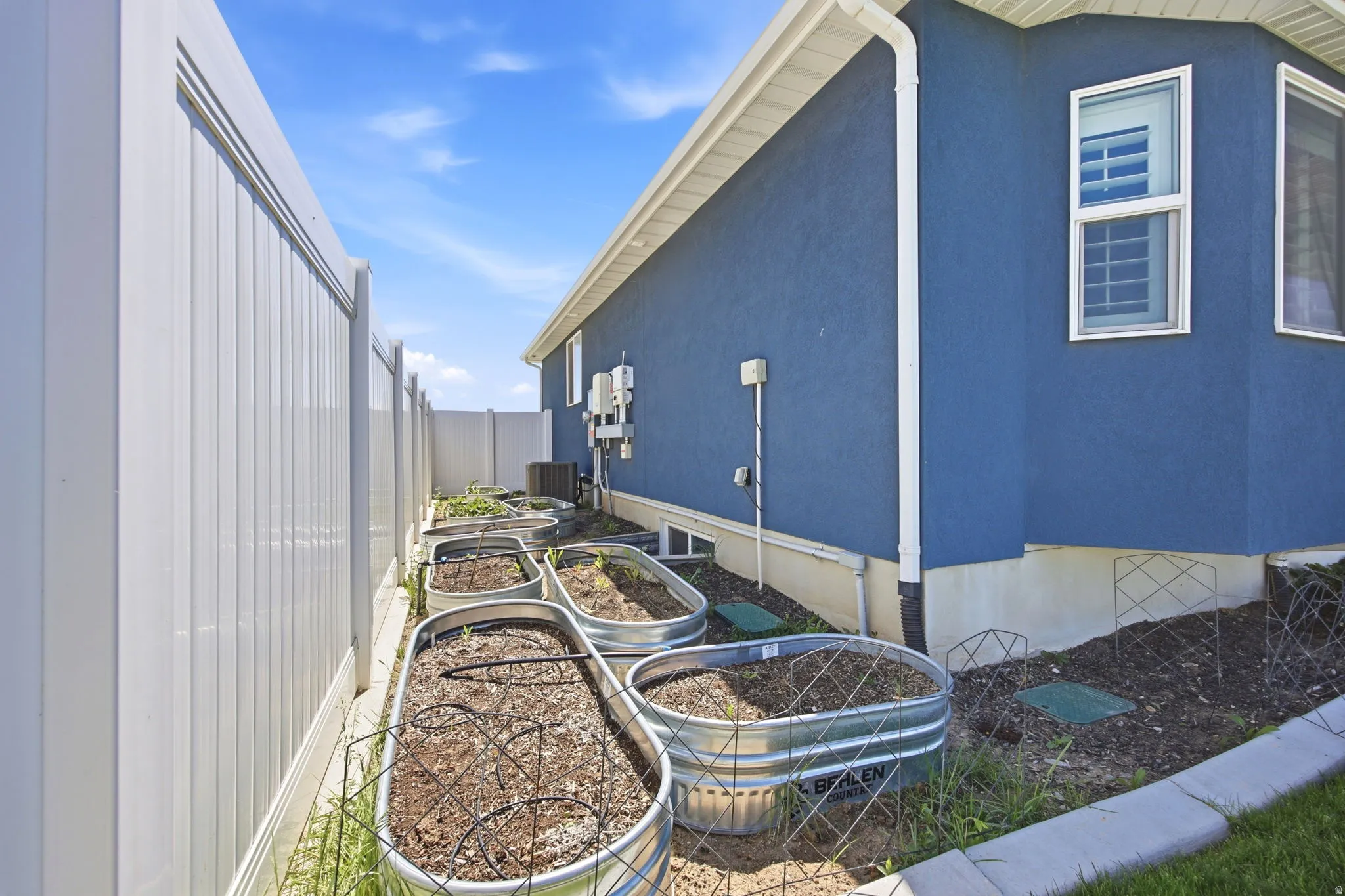 Side yard featuring multiple metal raised garden beds, a white vinyl privacy fence, and a stucco exterior