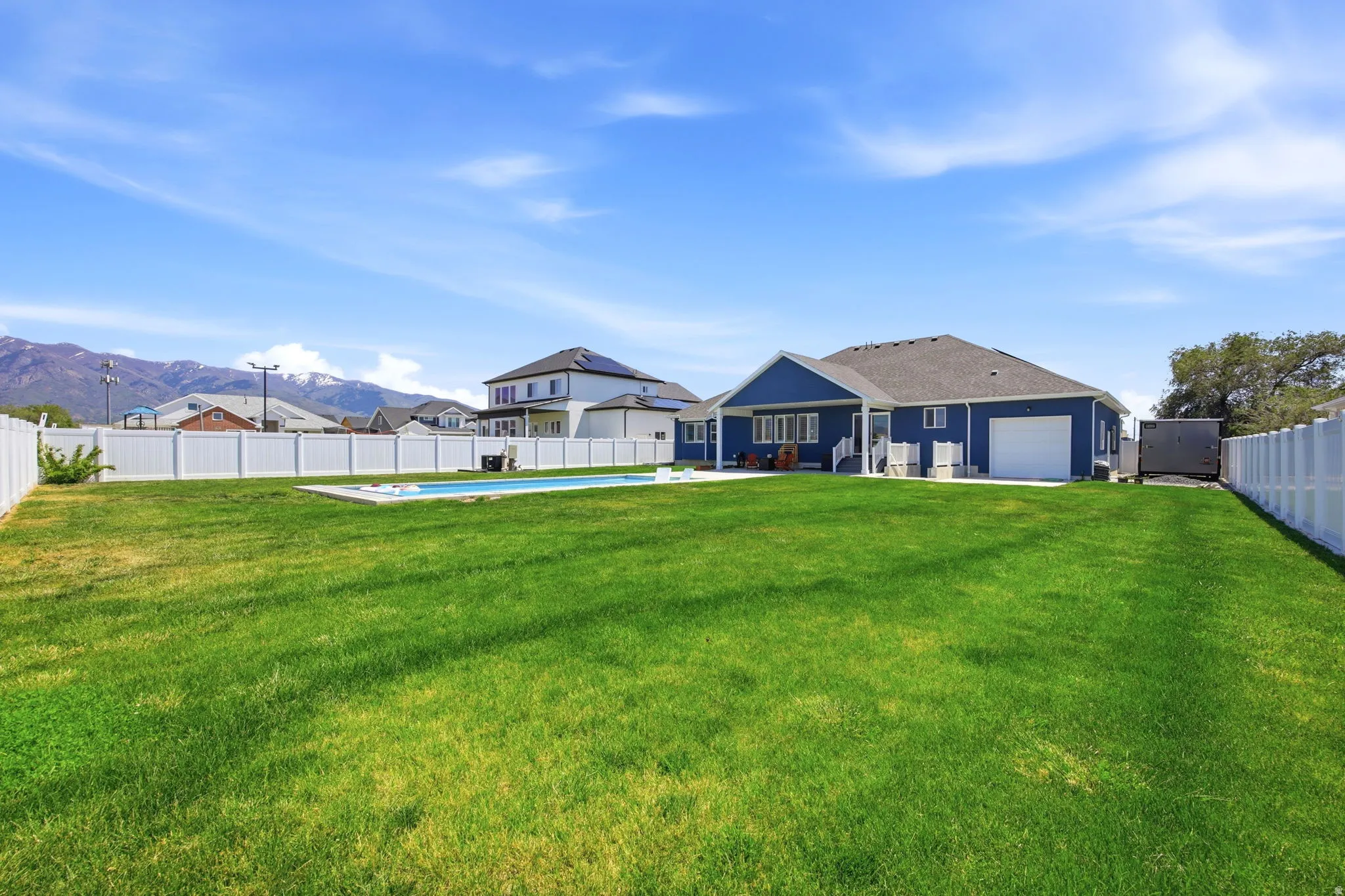 Spacious green lawn featuring a white privacy fence, an in-ground swimming pool, and a blue exterior home with a white garage door