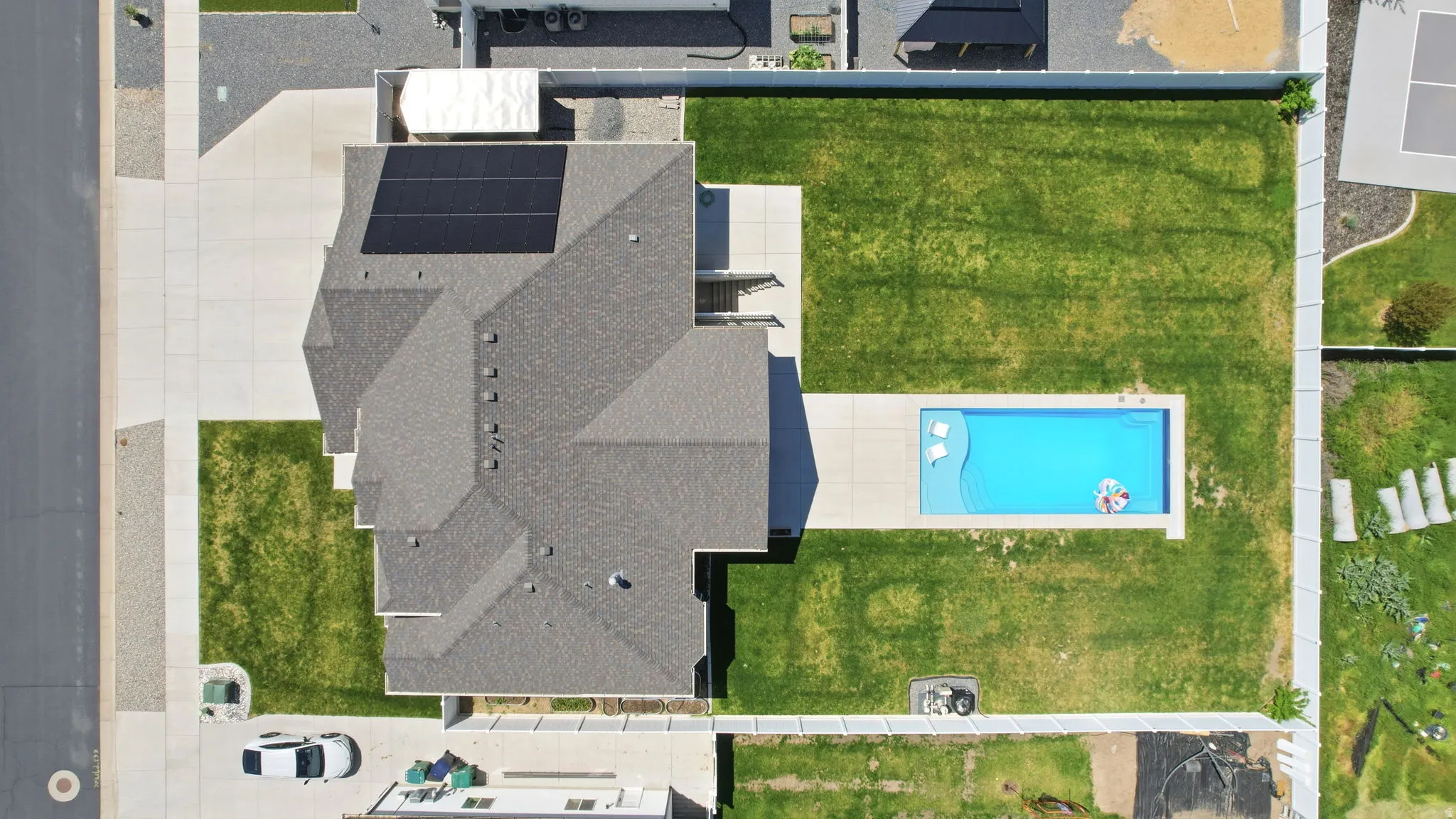 Expansive backyard featuring an in-ground swimming pool with surrounding concrete patio, manicured lawn, and perimeter fencing