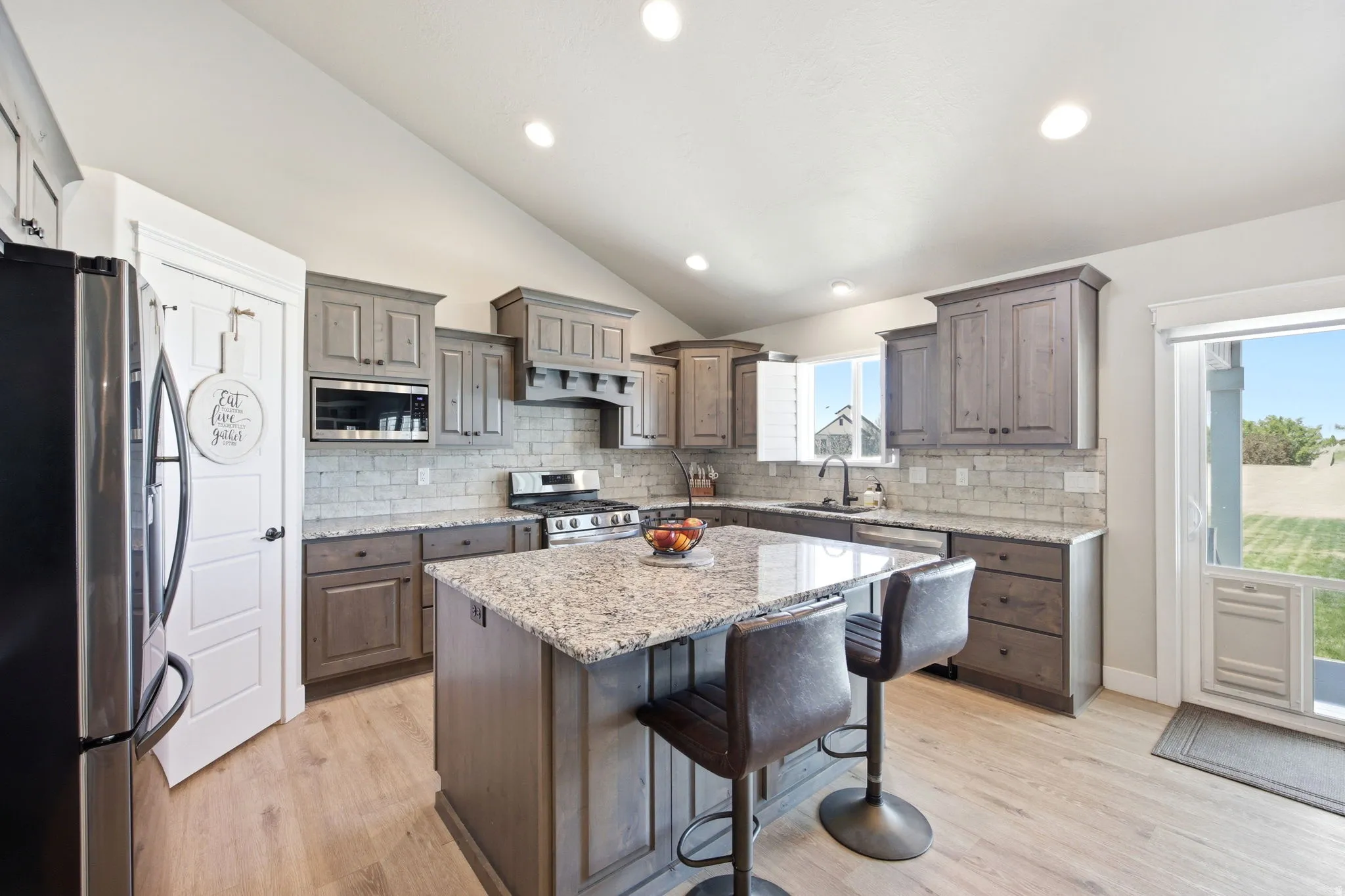 Kitchen featuring a central island with granite countertop, recessed lighting, wood-finish flooring, a full suite of stainless steel appliances, and a tiled backsplash