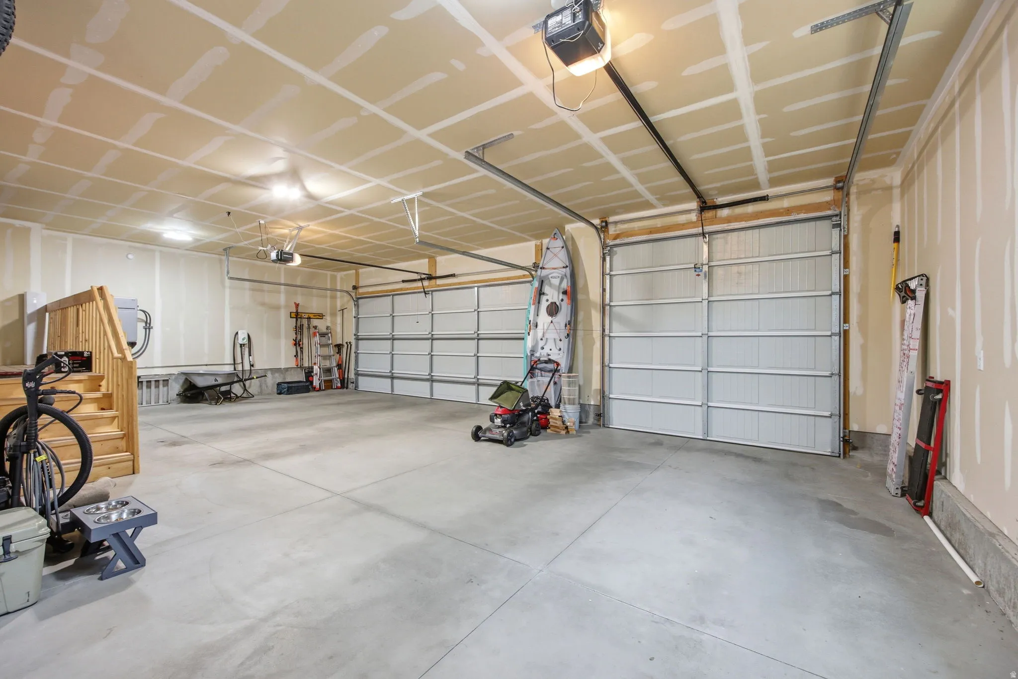 Spacious garage featuring two overhead doors with automatic openers, a concrete floor, and an interior staircase with wood-finish railings
