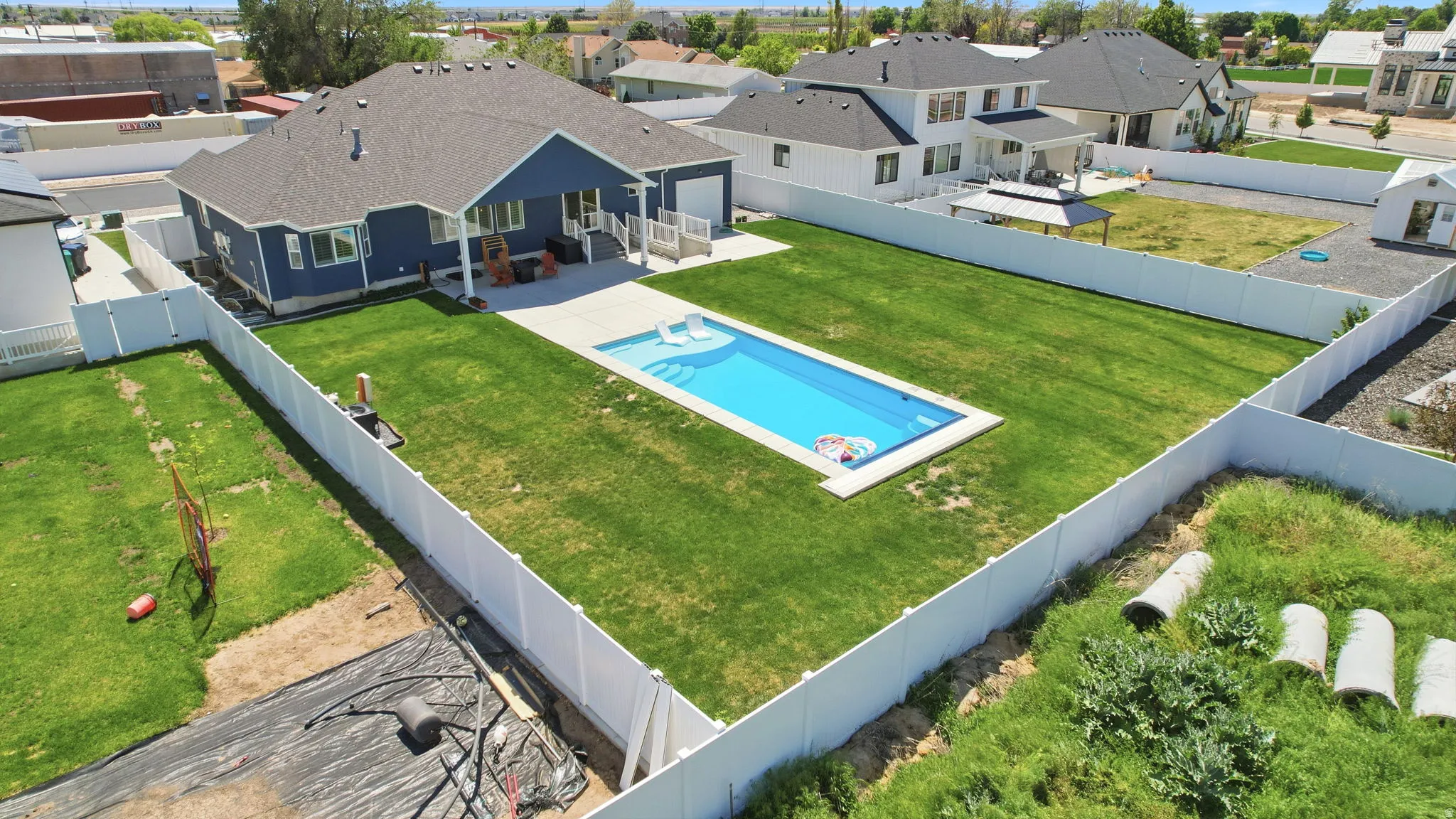Expansive backyard featuring a rectangular in-ground swimming pool with white coping, a surrounding green lawn, and full white privacy fencing
