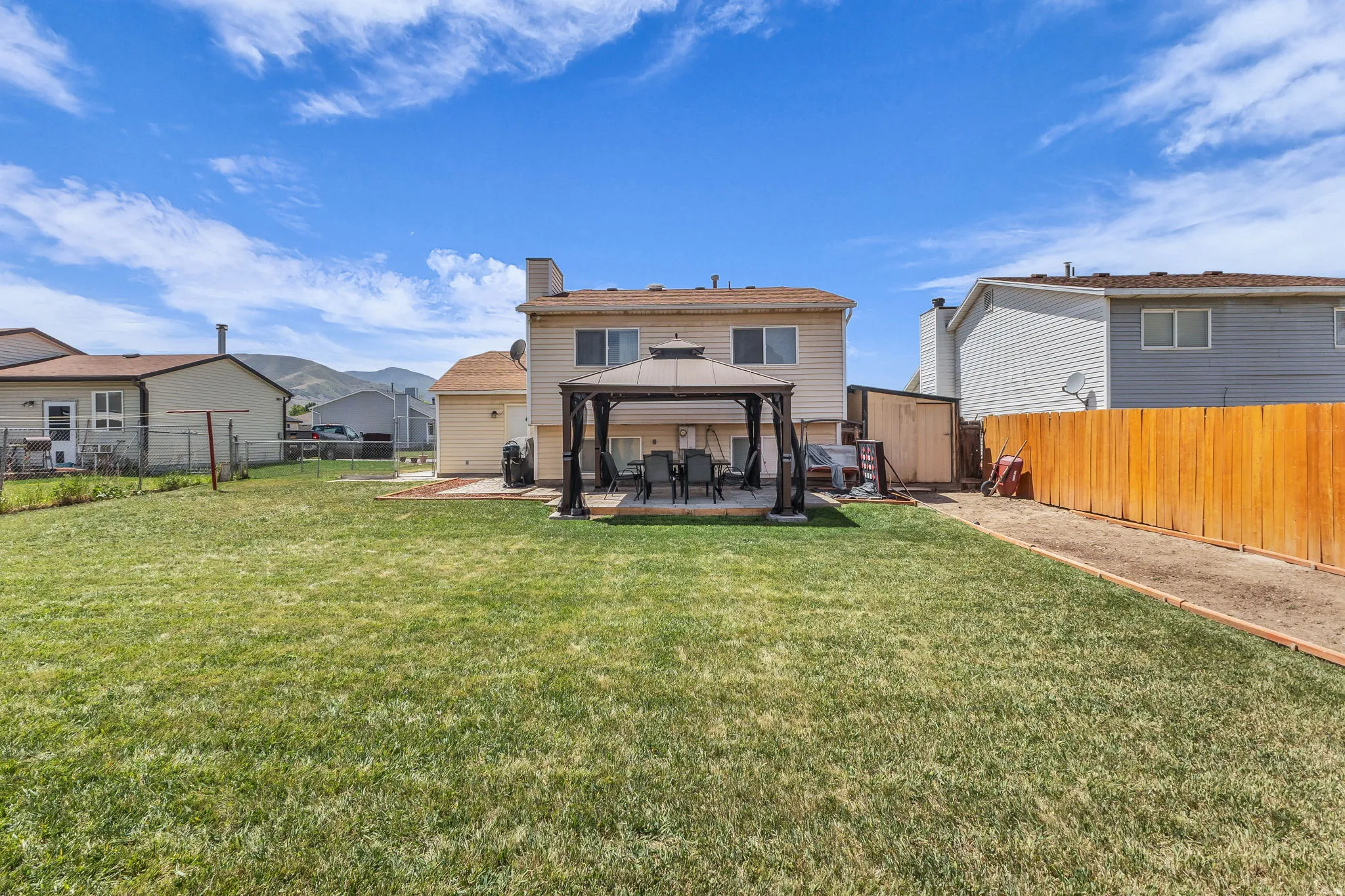 Expansive backyard featuring a large green lawn, a raised wooden deck with a gazebo, and a privacy fence