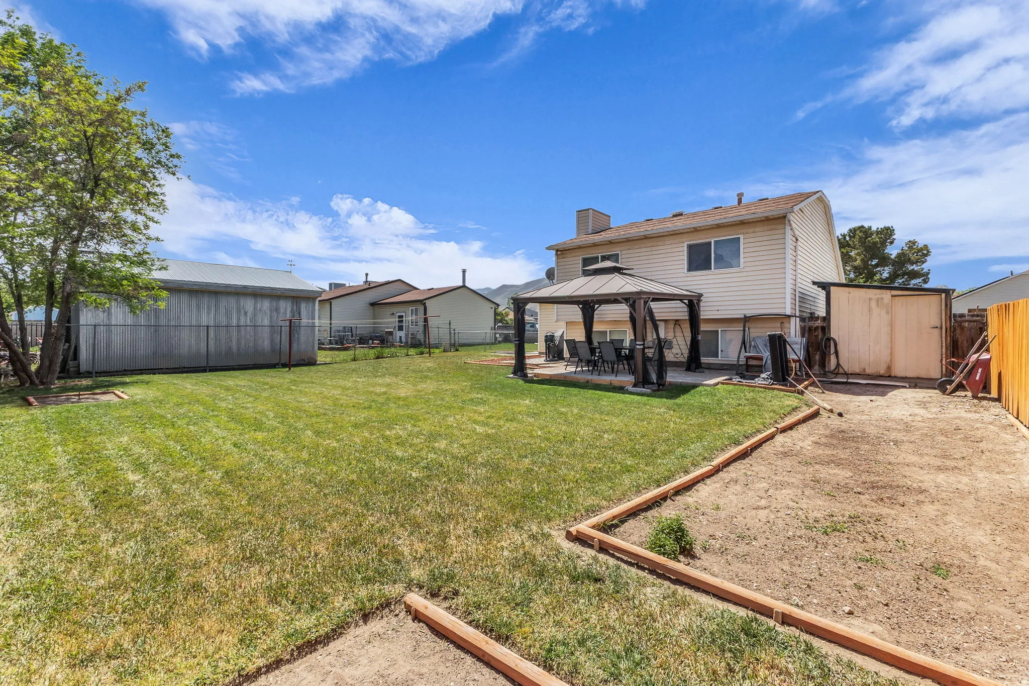 Spacious backyard featuring a large lawn area, an outdoor gazebo on a paved patio, and a dedicated garden bed