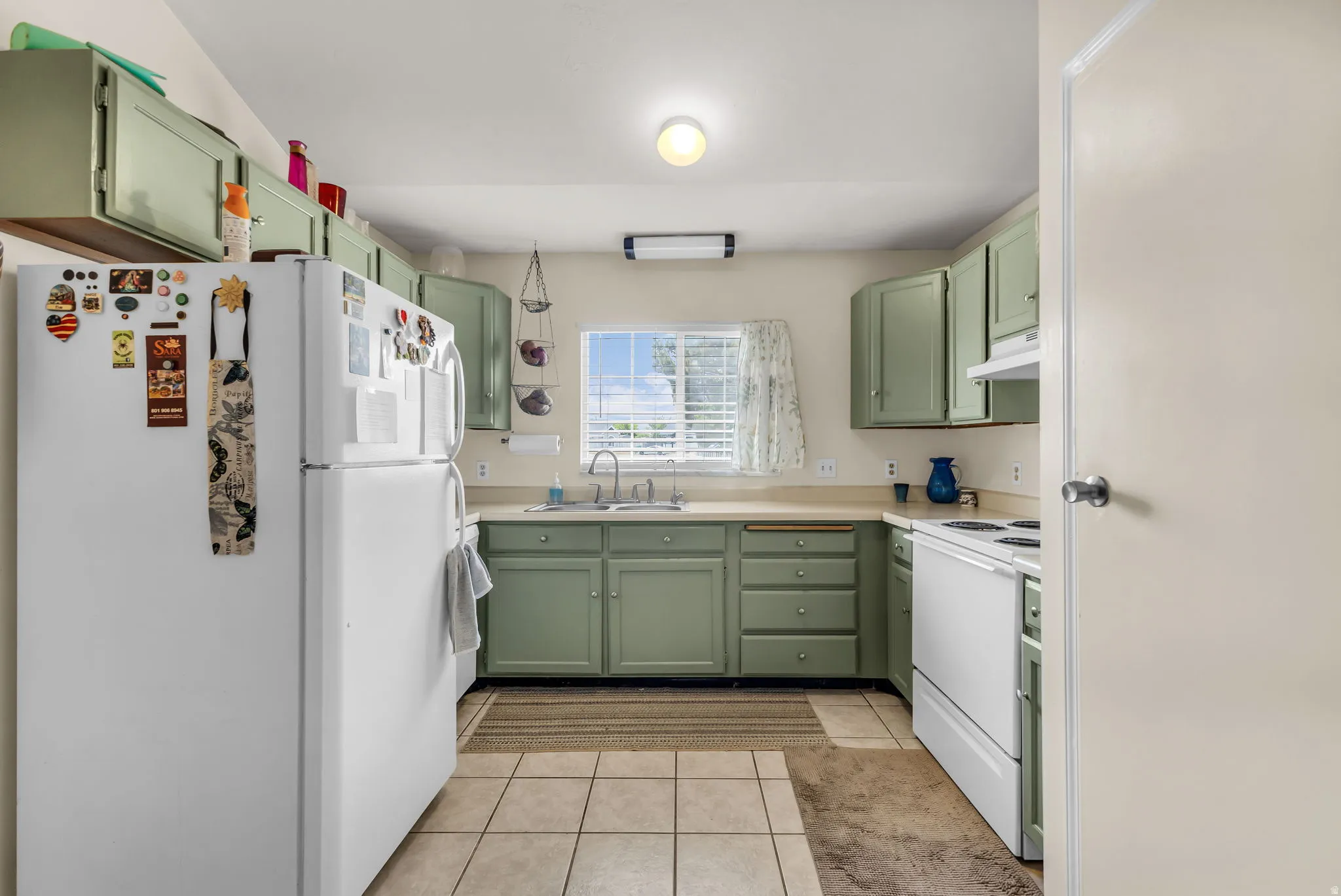 Kitchen featuring green cabinetry, light-toned countertops, and a window with blinds