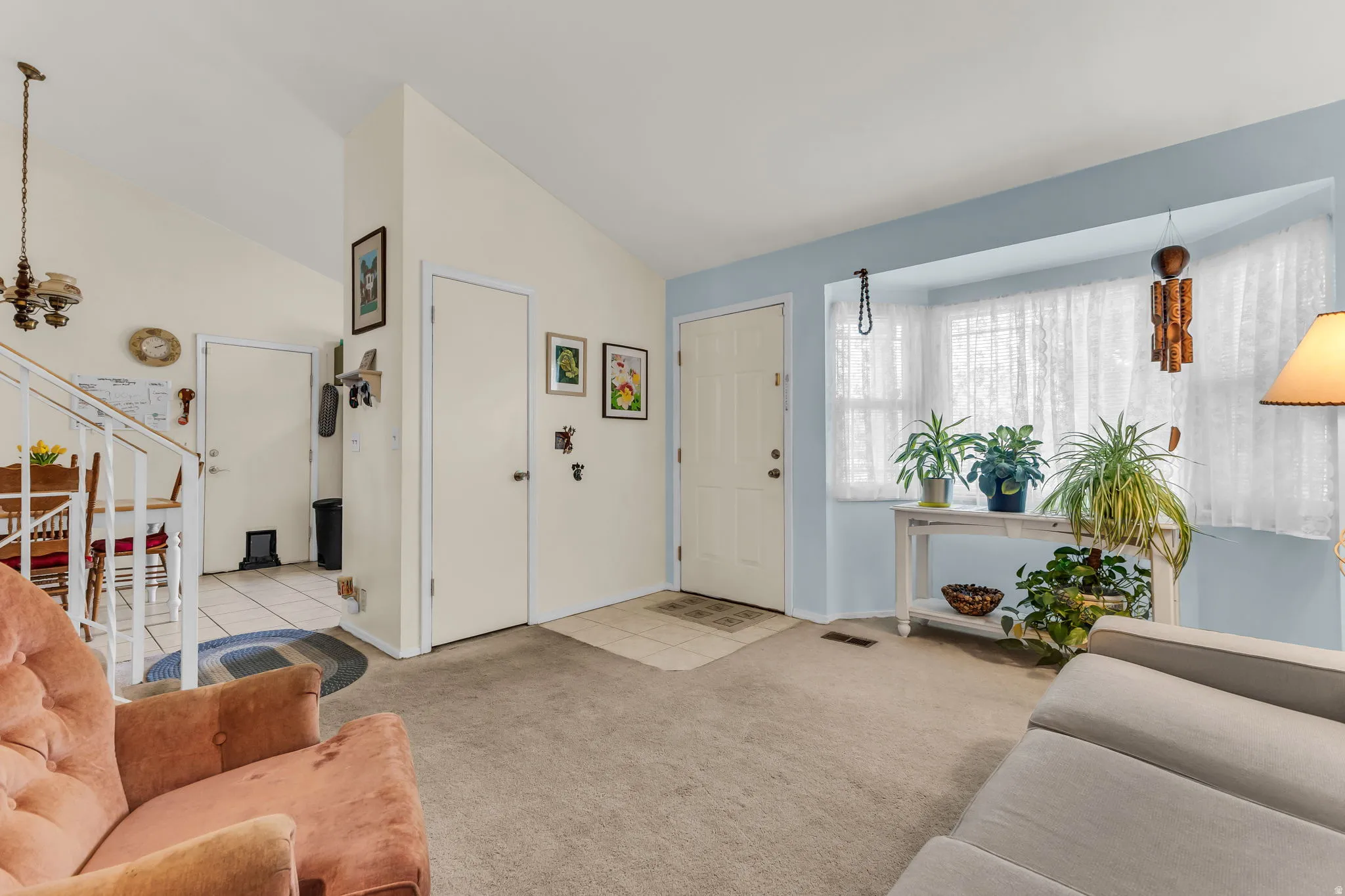 Living space featuring vaulted ceilings, a bay window with lace curtains, and light-colored carpeting