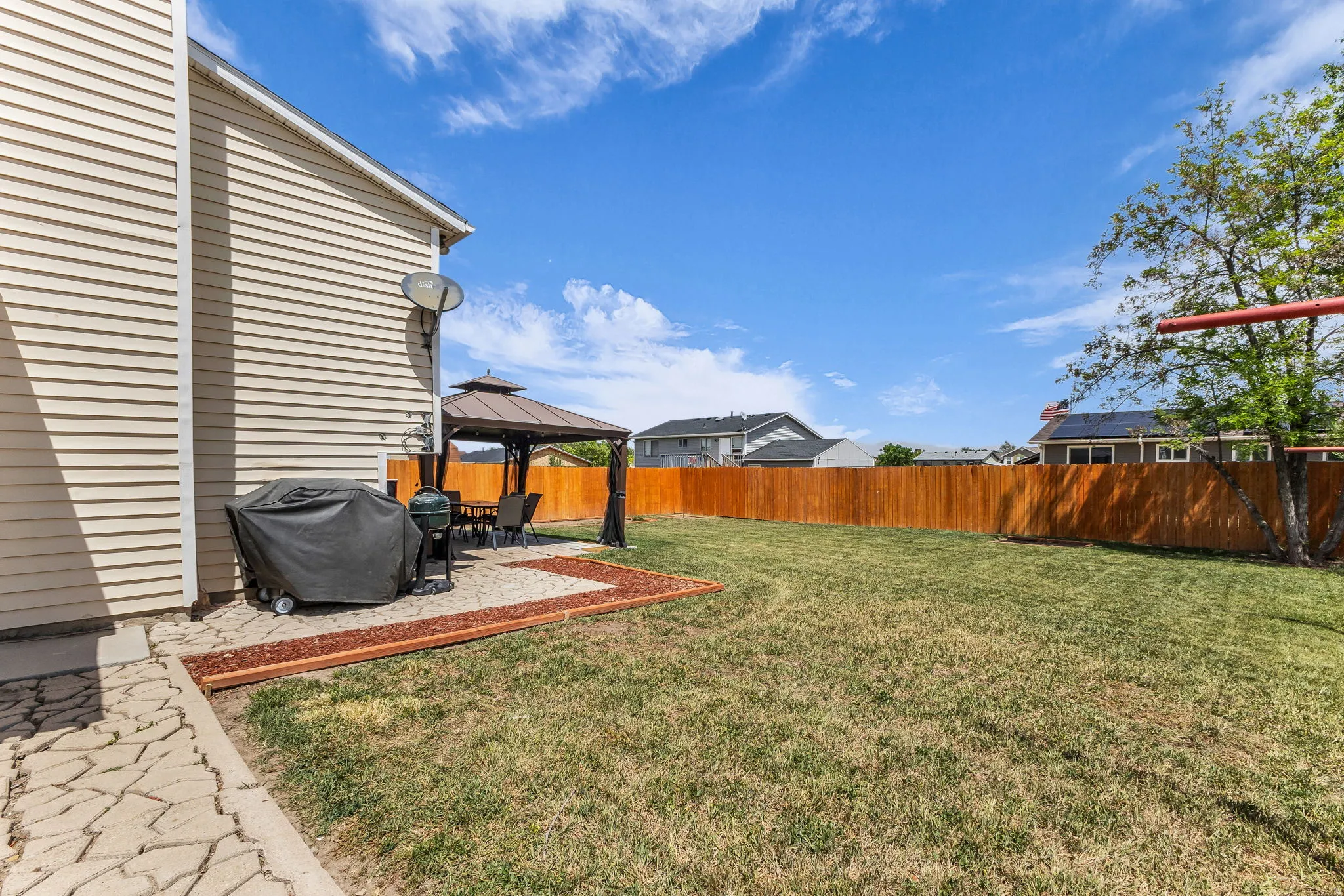 Expansive backyard featuring a manicured lawn, a full wooden privacy fence, and a paved patio area