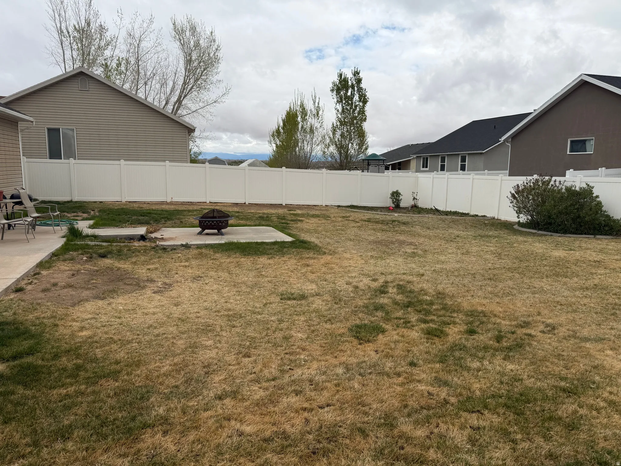 Expansive backyard featuring a white vinyl privacy fence, a concrete patio, and a dedicated concrete pad