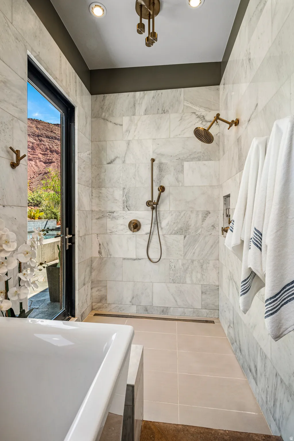 Spacious shower with large format tile walls, linear drain, and bronze-finish fixtures