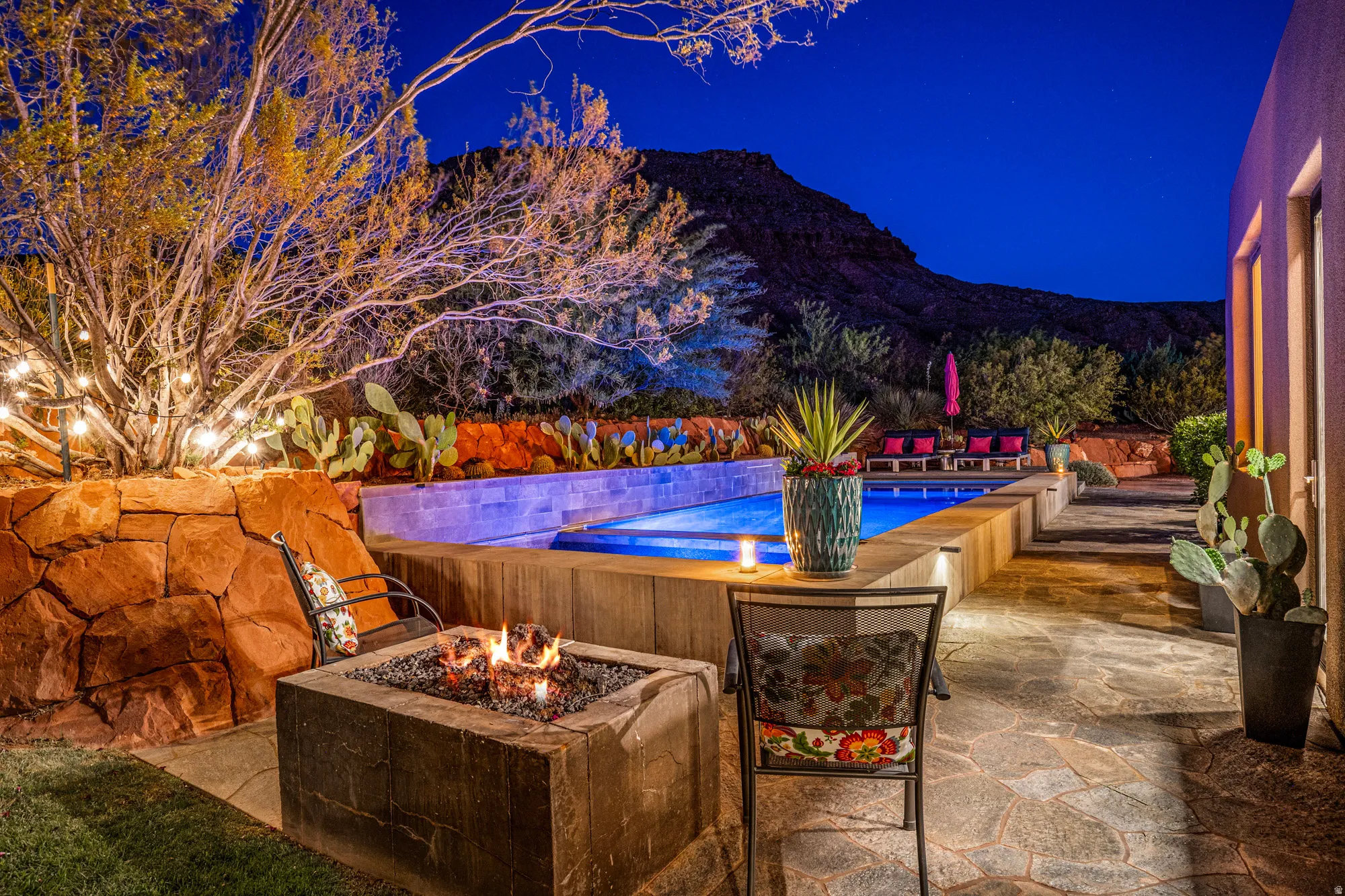 Outdoor living area featuring a built-in fire pit, a swimming pool with integrated lighting, and natural stone patio flooring