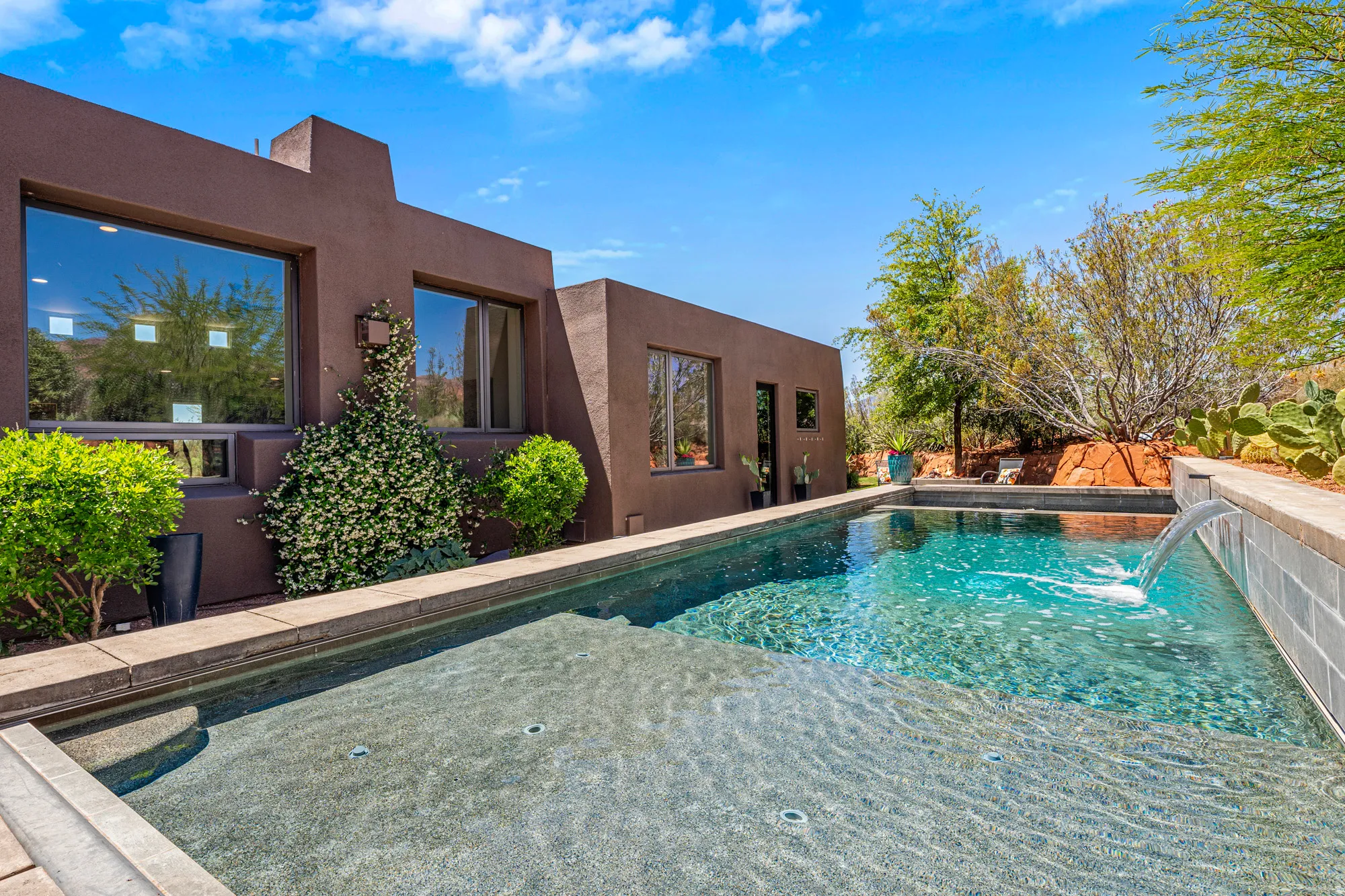 Contemporary brown stucco exterior with multiple windows, an integrated swimming pool, and an in-pool spa