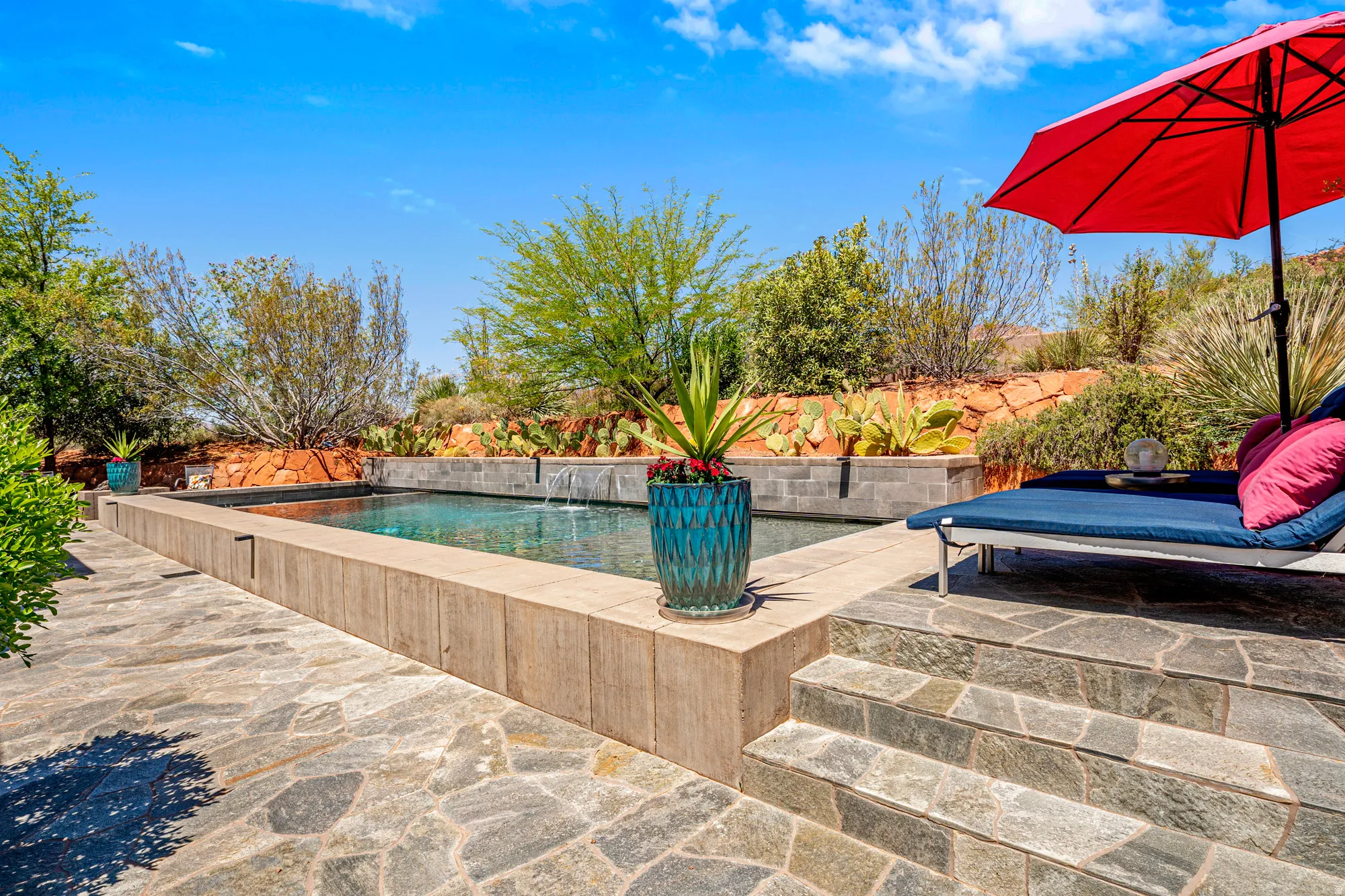 Rectangular swimming pool with water feature, surrounded by flagstone paving and a raised planter bed