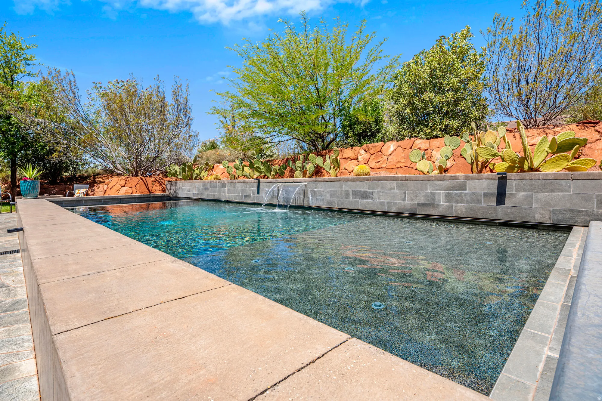 Rectangular swimming pool with water features, surrounded by stone coping and a block retaining wall