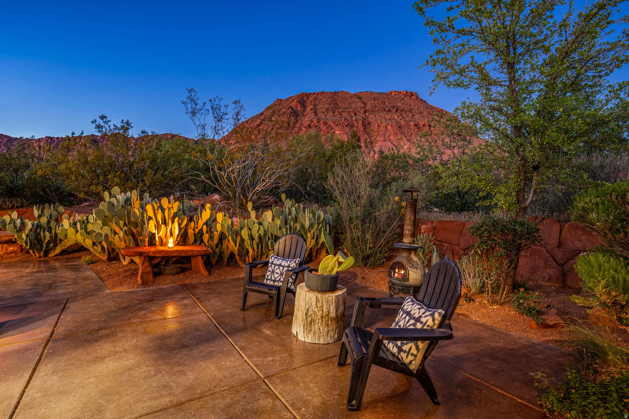 Spacious outdoor patio with concrete flooring, surrounded by desert landscaping and a stone retaining wall