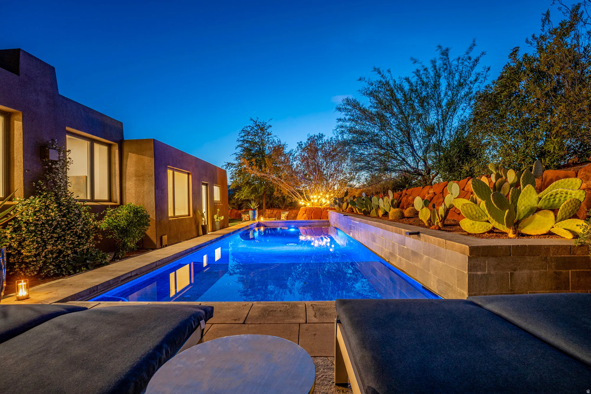 Illuminated swimming pool with integrated spa, bordered by a stone-clad raised planter featuring desert landscaping
