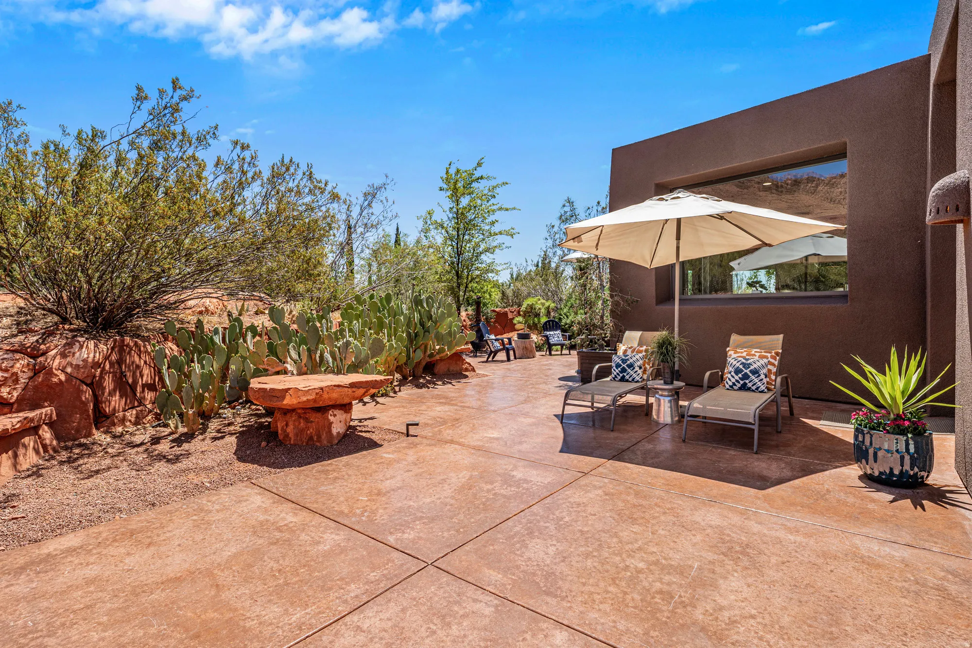 Expansive patio featuring scored concrete flooring, a desert-adapted landscape with rock formations and cacti, and a recessed window