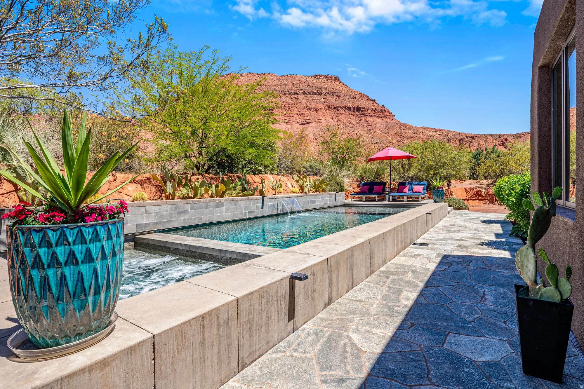 Outdoor oasis featuring a linear pool with an integrated spa, natural stone patio, and a backdrop of red rock formations