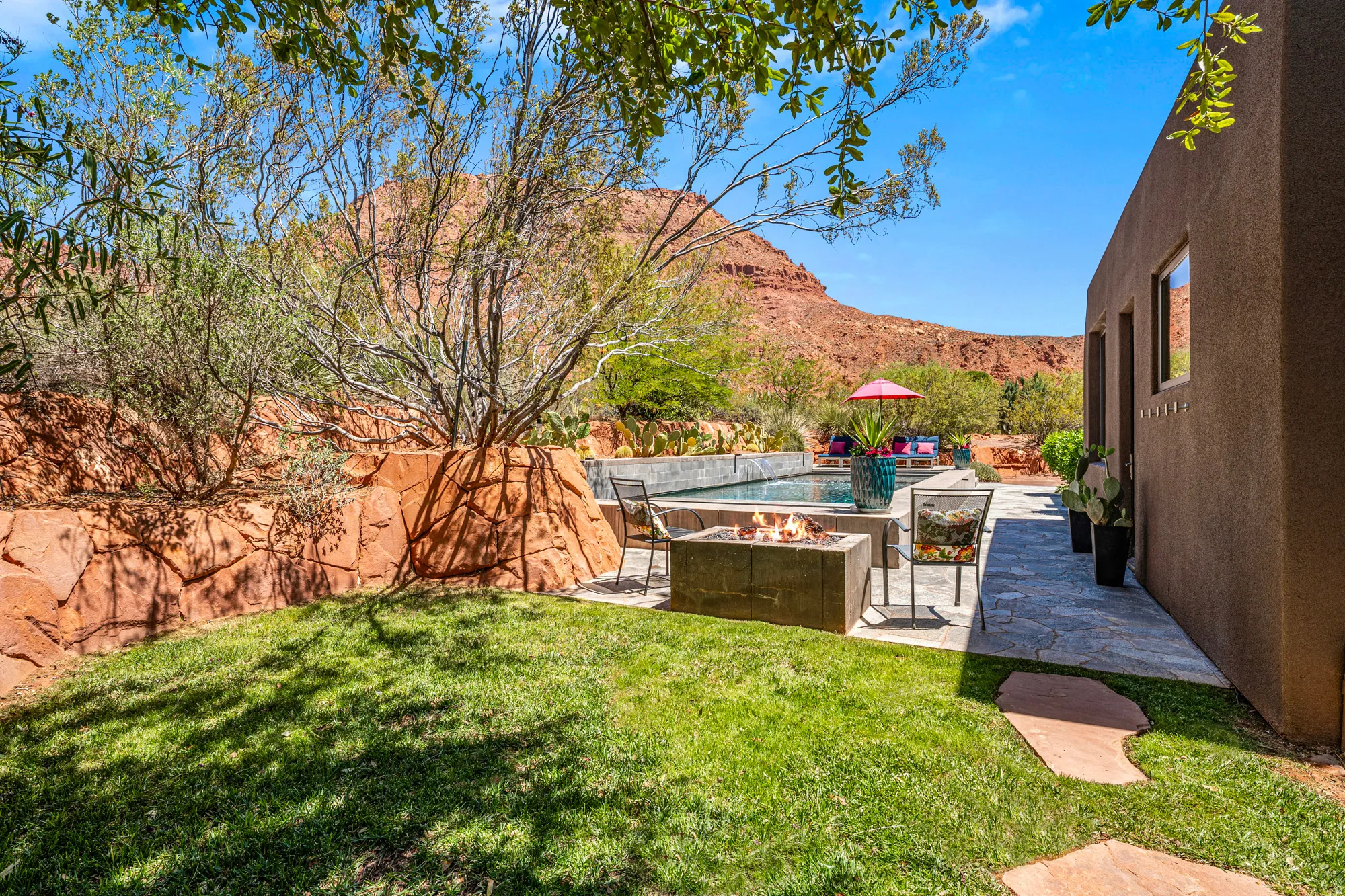 Expansive backyard featuring a manicured lawn, stone paver patio, built-in fire pit, and a swimming pool